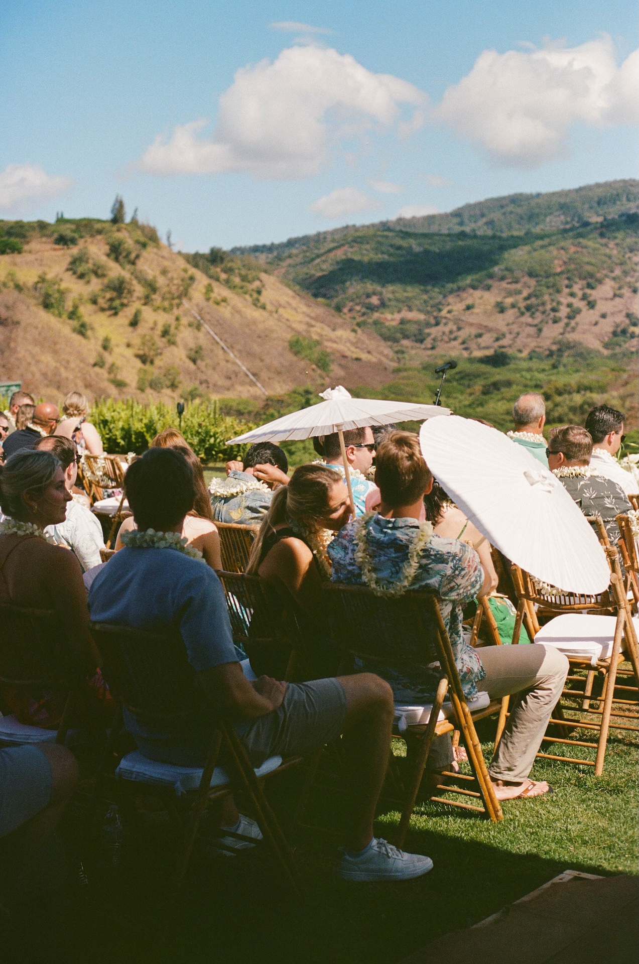 Guests sitting in folding chairs with white umbrellas while watching the ceremony at the hawaii destination wedding 