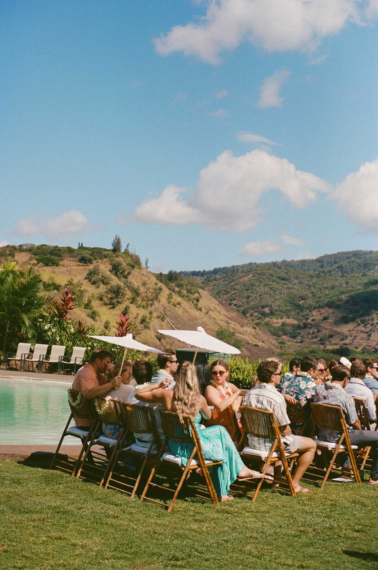 Guests sitting in folding chairs with white umbrellas while watching the ceremony at the hawaii destination wedding 