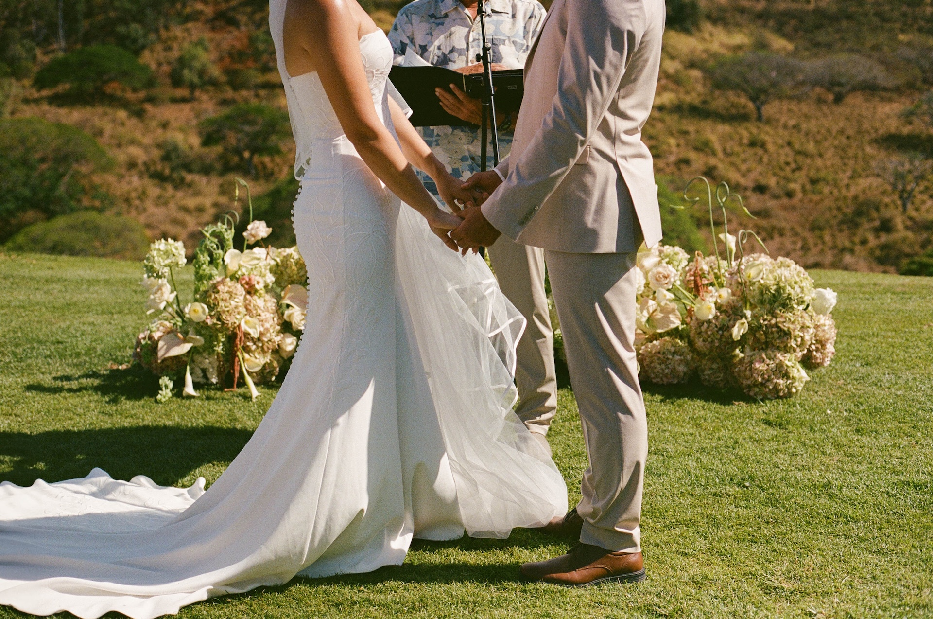 Film photo of the bride and groom holding hands at the alter, shot from the shoulders down.