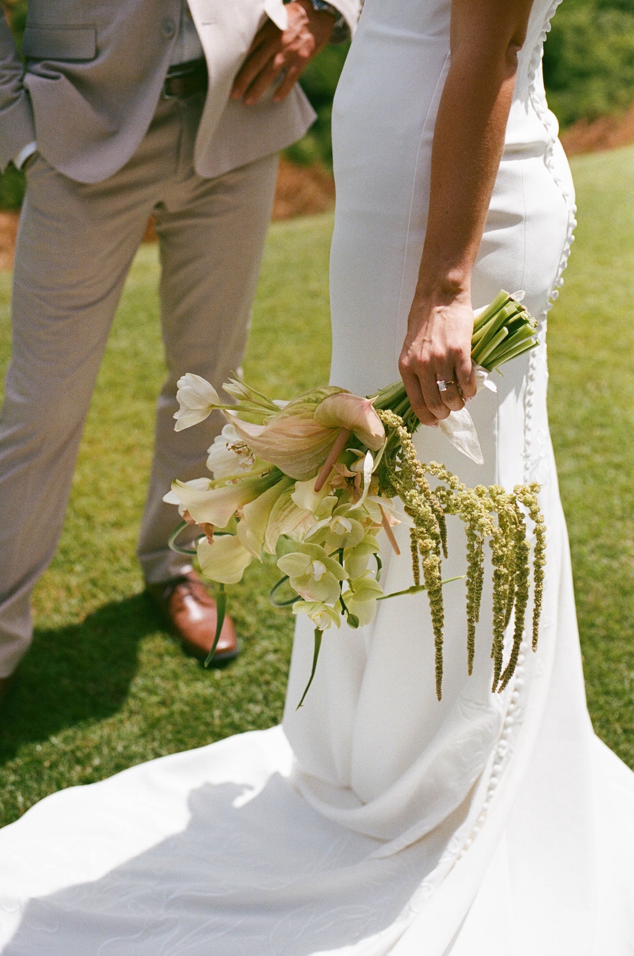 Detail photo of the bride and groom from the hip down, the bride holding her bouquet and the groom has a hand on his hip.