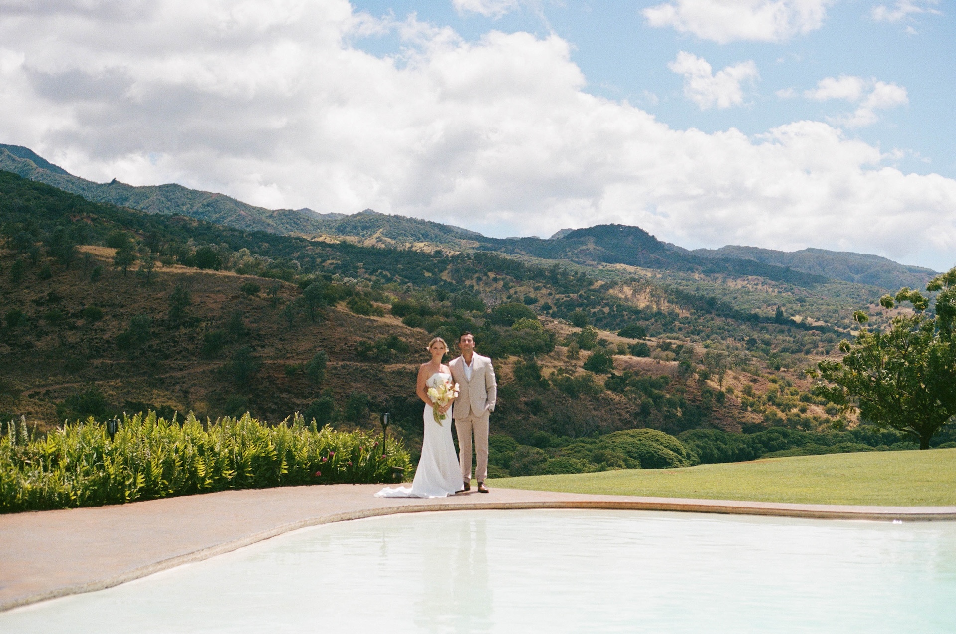 Bride and groom standing across the pool, with the mountains in the background for their hawaii destination wedding.