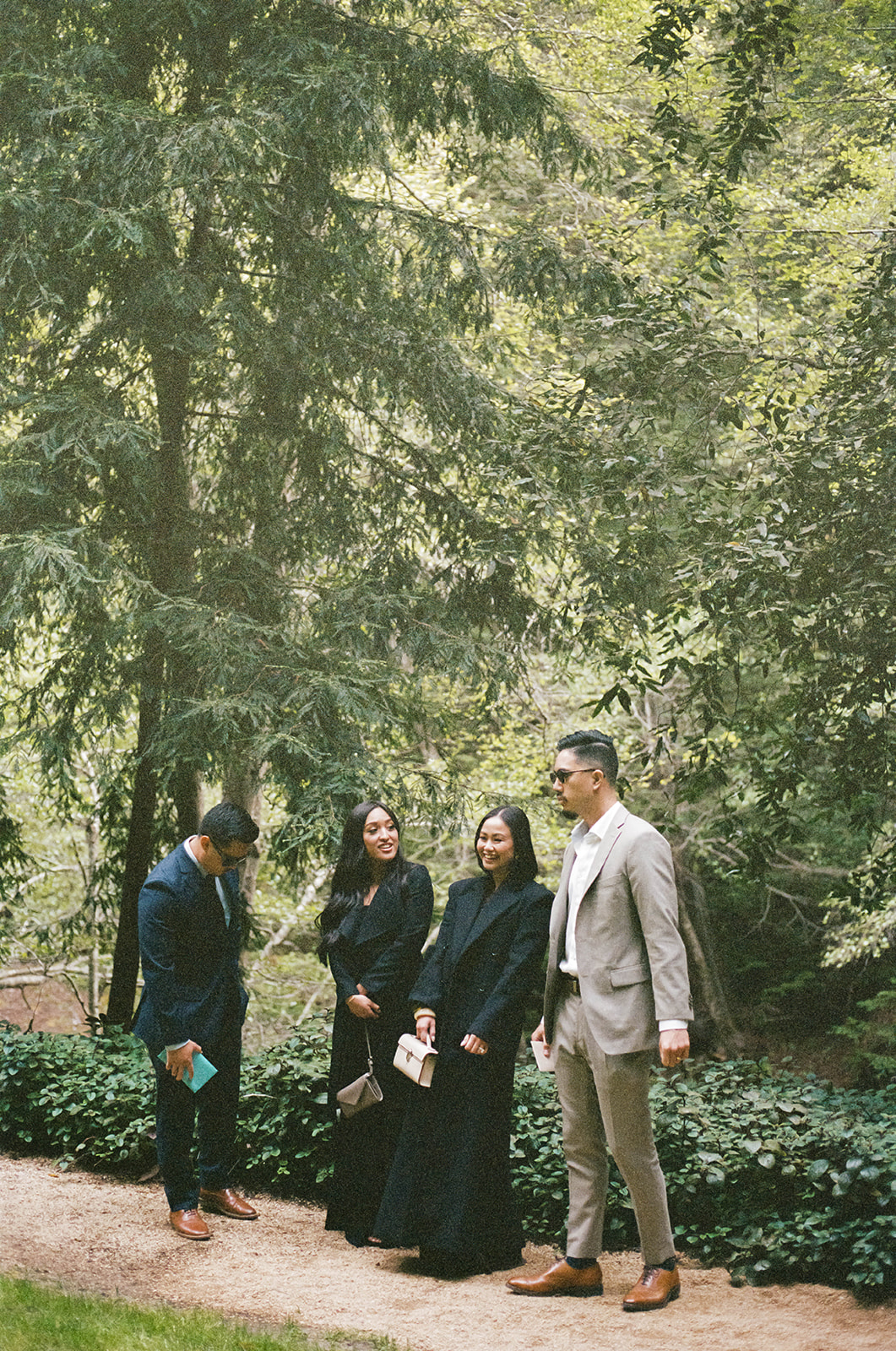 Guests walking along a forest path before the wedding ceremony, dressed in formal attire surrounded by lush greenery.

