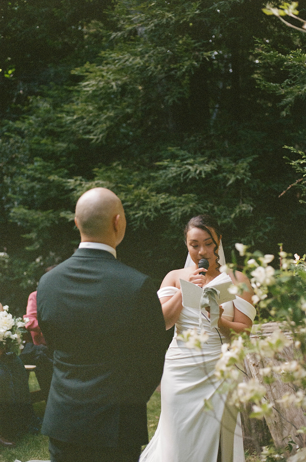 Bride reading her vows during their ceremony, standing across from her groom with tall pines behind her during their Big Sur Wedding.