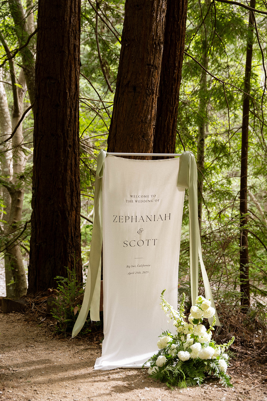 White welcome sign with green ribbon greeting guests to Zephaniah and Scott’s wedding in Big Sur.