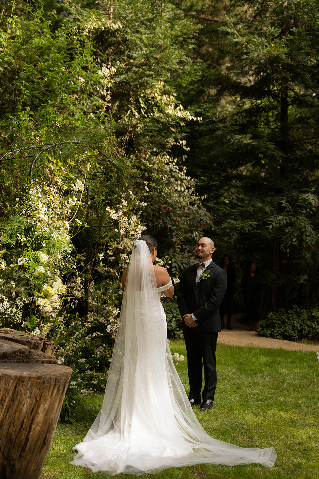 Bride facing groom under a floral arch surrounded by greenery during their Big Sur wedding.