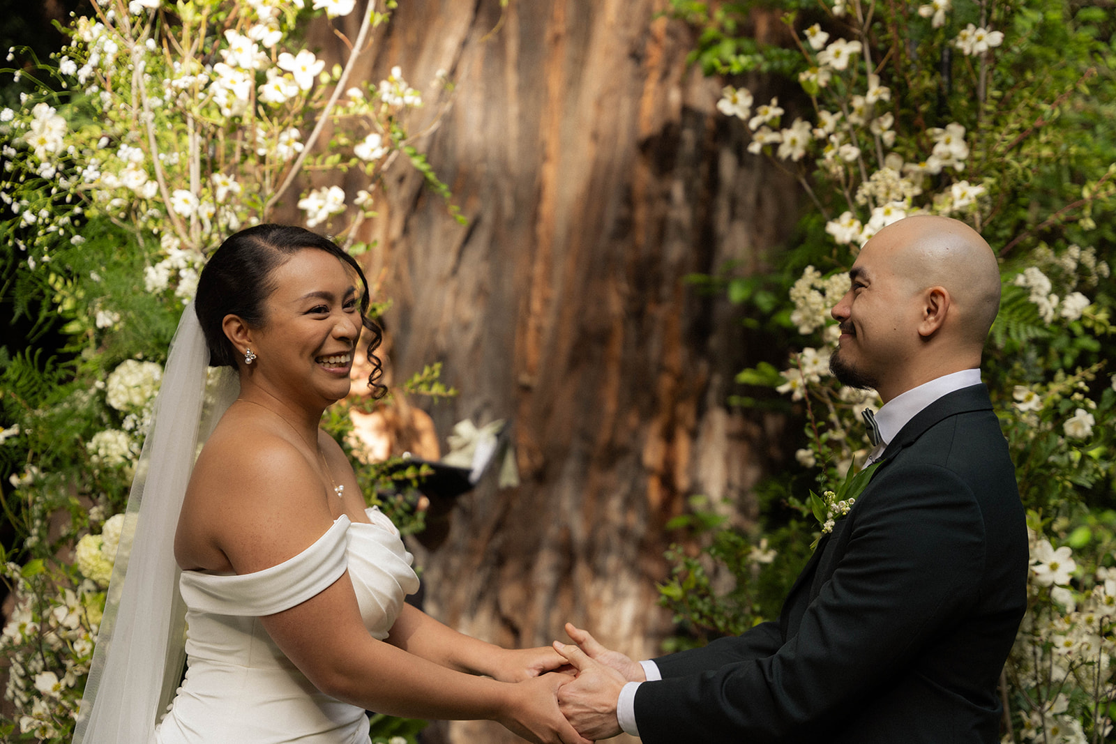Bride and groom holding hands and smiling during their Big Sur wedding ceremony in the redwoods.