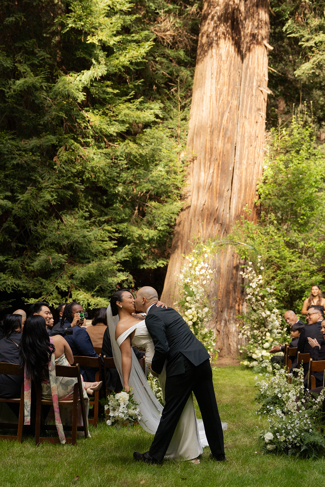 Bride and groom share a kiss at the altar surrounded by redwoods at their Big Sur wedding.