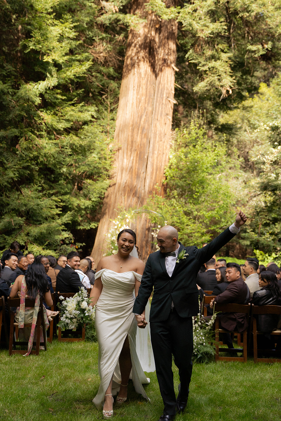 Bride and groom walking back up the aisle after their ceremony surrounded by guests at a redwood grove Big Sur wedding venue.