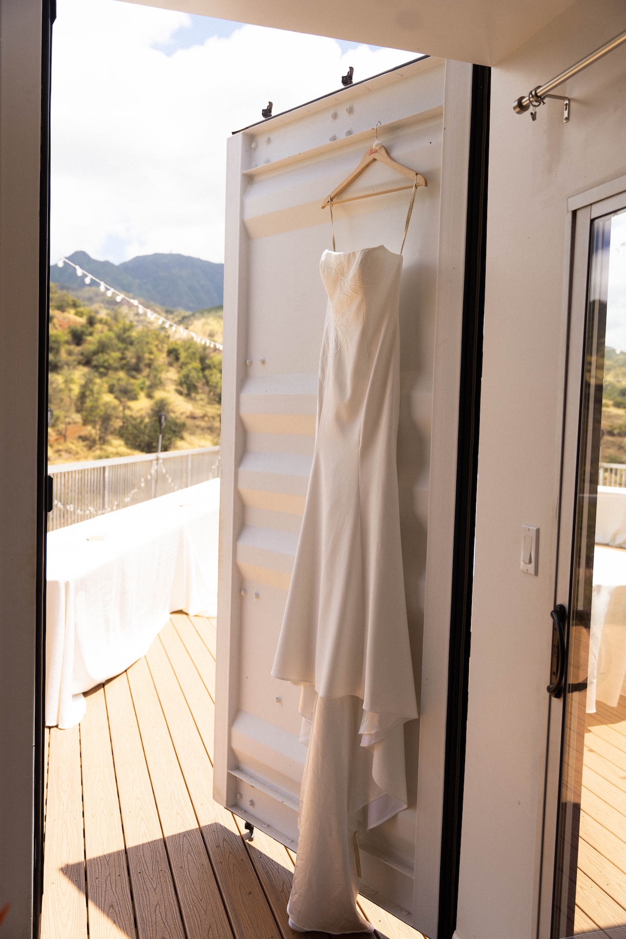 The bride’s strapless wedding gown hanging on a wooden hanger in the getting-ready space.

