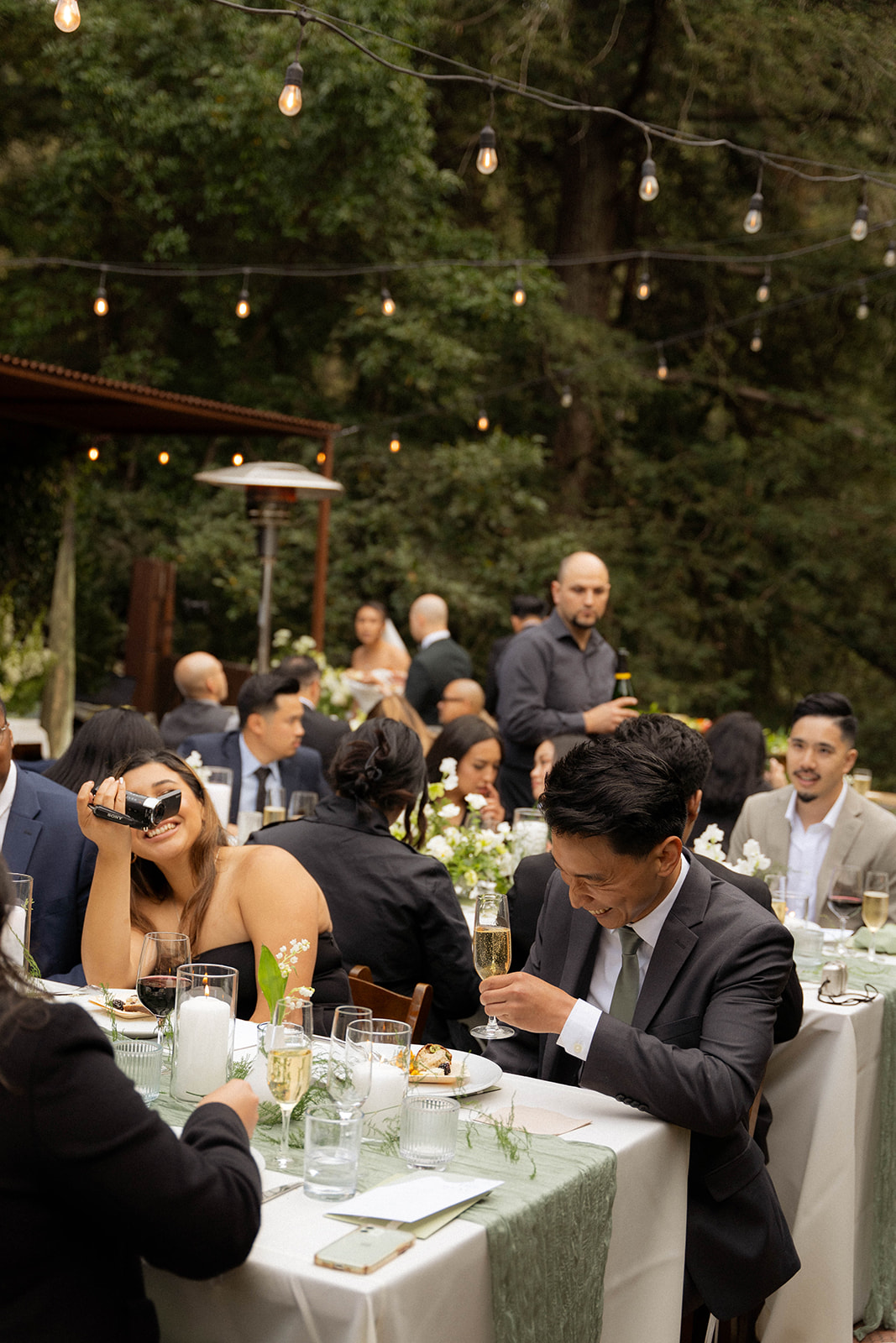 Wedding guests laugh and chat under string lights at an outdoor Big Sur wedding dinner.