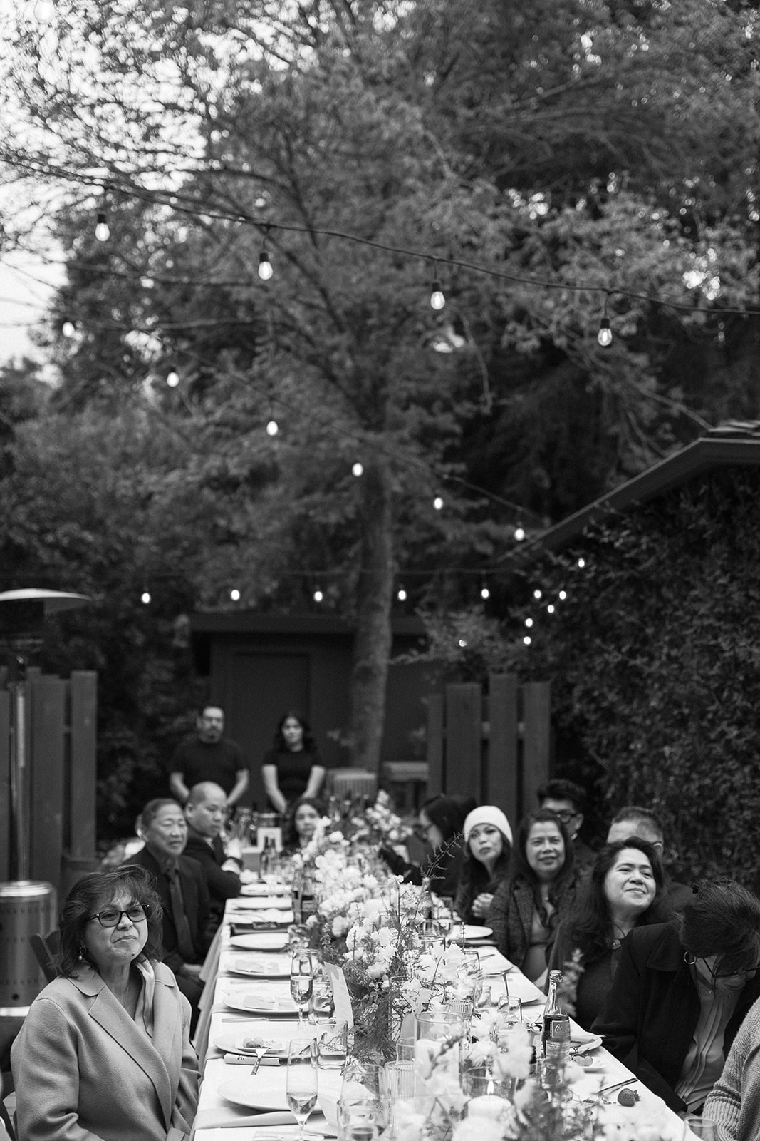 Guests seated at a long outdoor reception table under twinkling lights at a forest wedding in Big Sur.