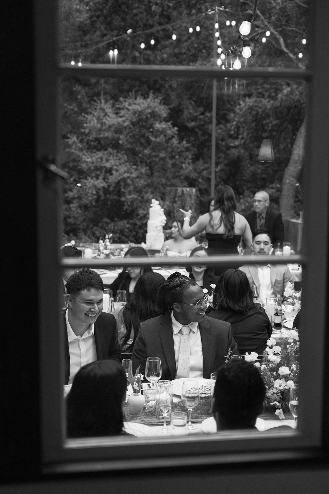 Wedding guests laughing and enjoying dinner through a cabin window at an intimate Big Sur wedding reception.
