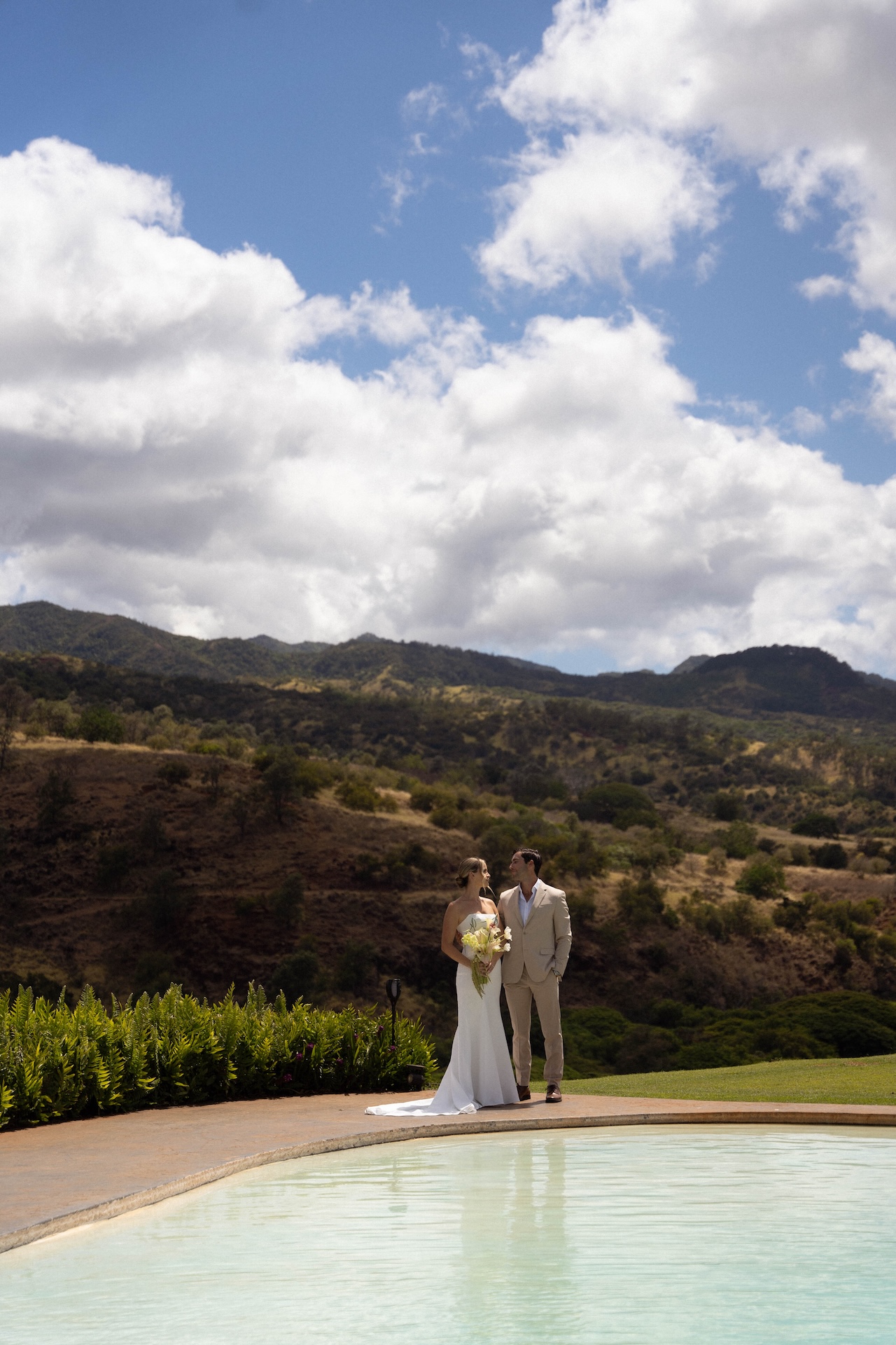 Couple standing by the pool at Kaʻala Vista with mountain views behind them during their Hawaii destination wedding.