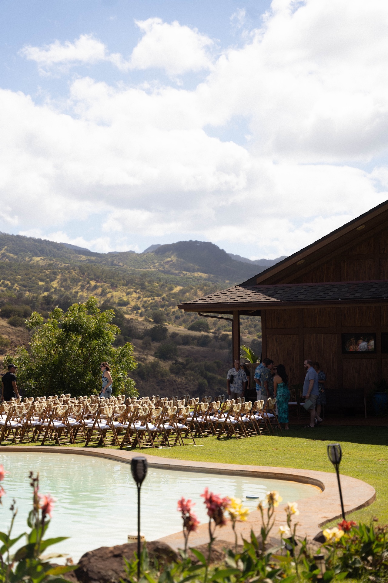 Guests gathering by the pool at Kaʻala Vista with tropical plants and the venue house in view.