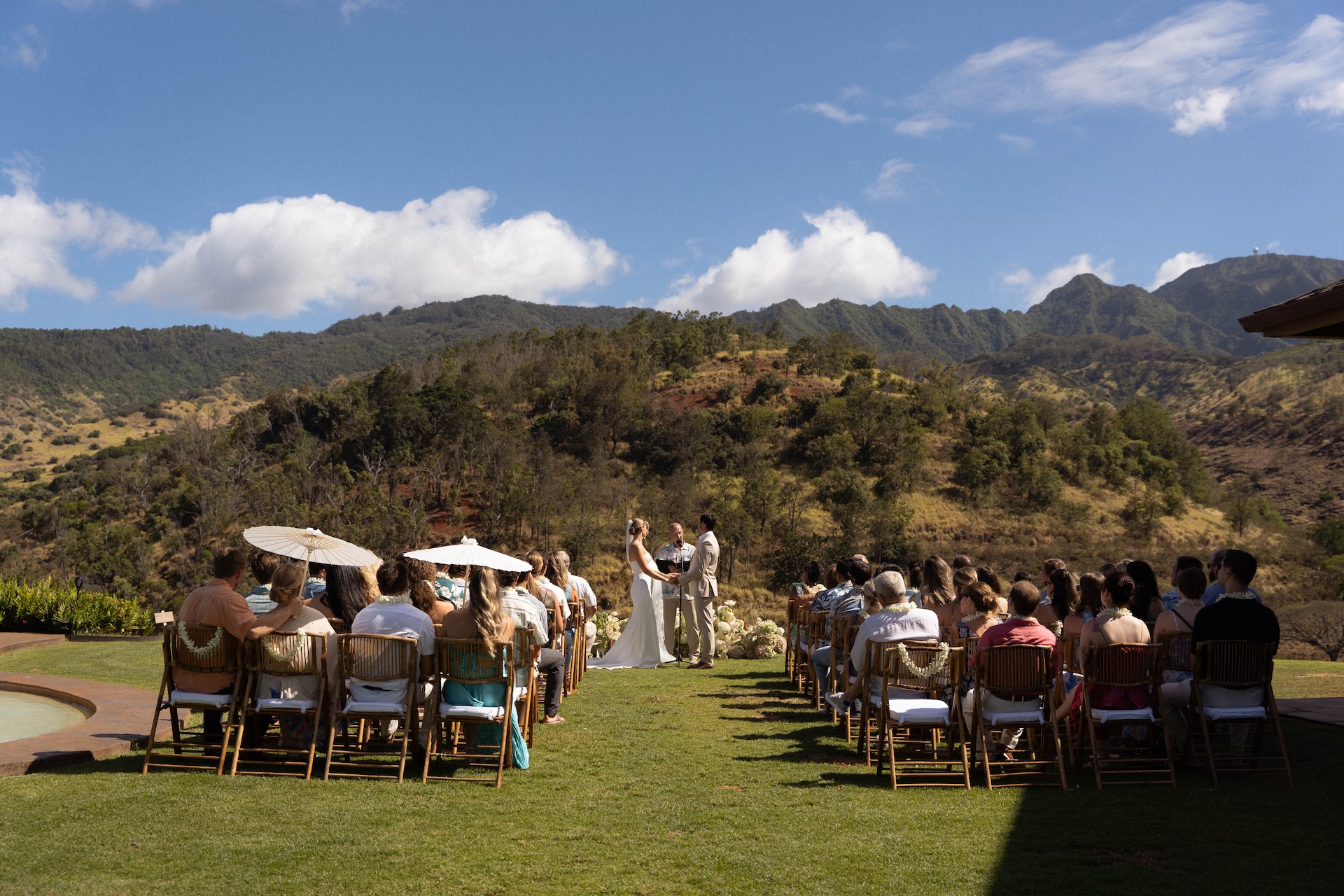 Wide shot of the outdoor wedding ceremony at Kaʻala Vista with guests seated and mountains in the background.