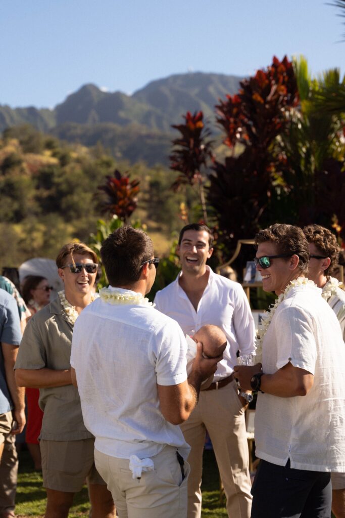Groom laughing with friends wearing leis and casual wedding attire during cocktail hour at Kaʻala Vista.