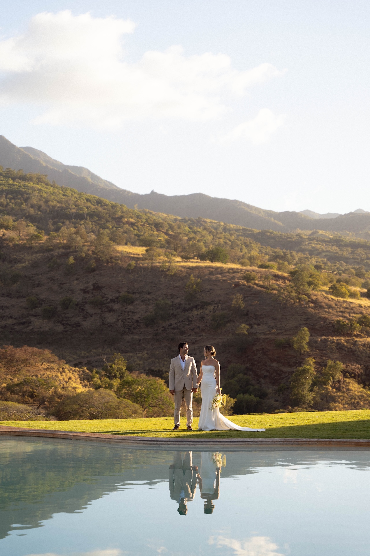 Back view of the couple walking by the pool at Kaʻala Vista during their Hawaii destination wedding golden hour portraits.