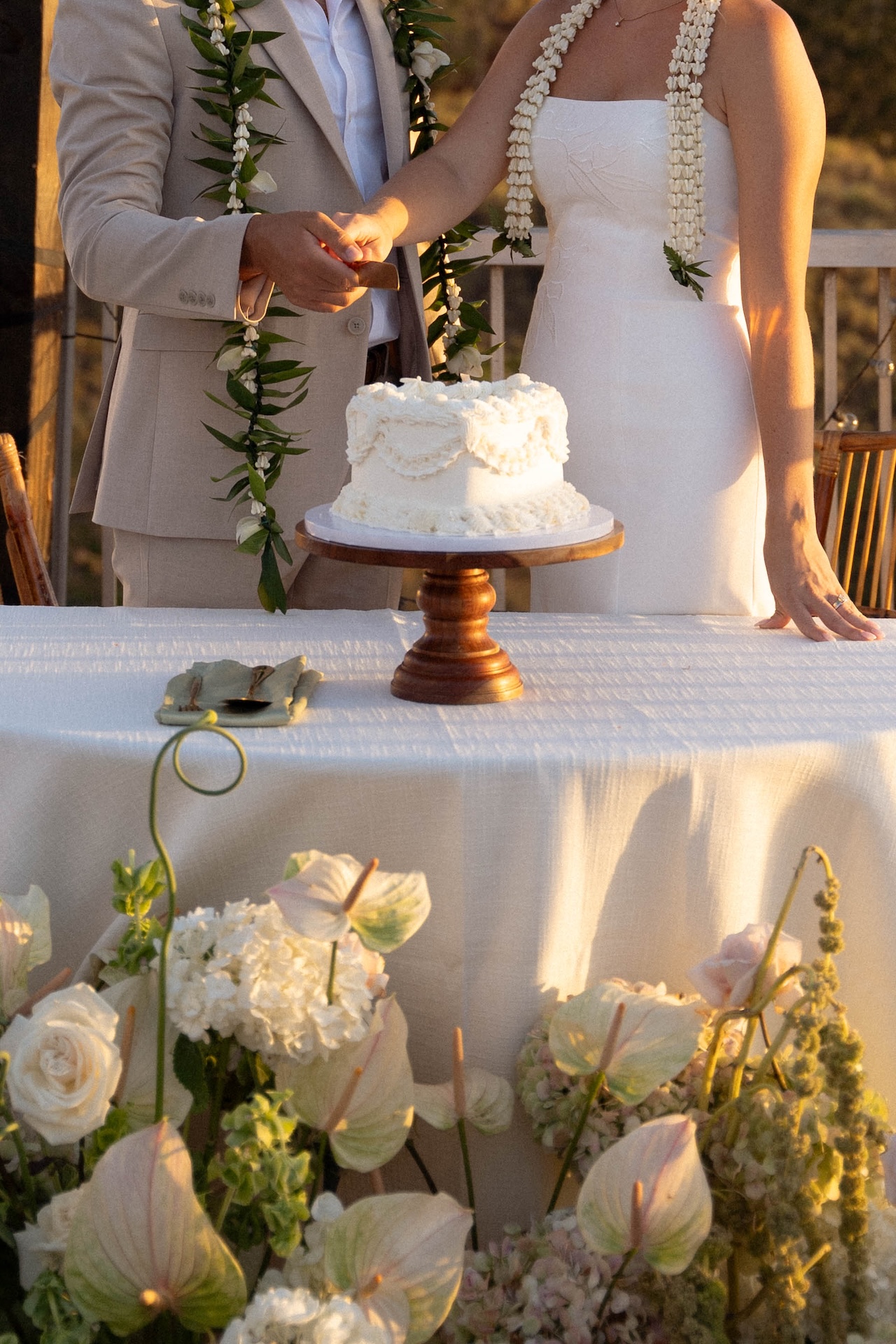 The bride and groom cut a small white cake adorned with decorative icing at their reception during there hawaii destination wedding.