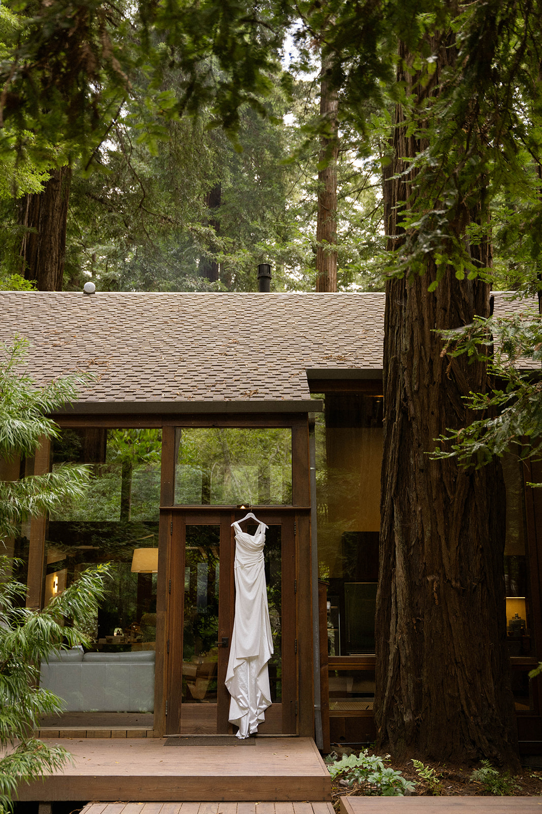 Bride’s wedding dress hanging on a wooden cabin door in the forest at a serene Big Sur wedding venue.