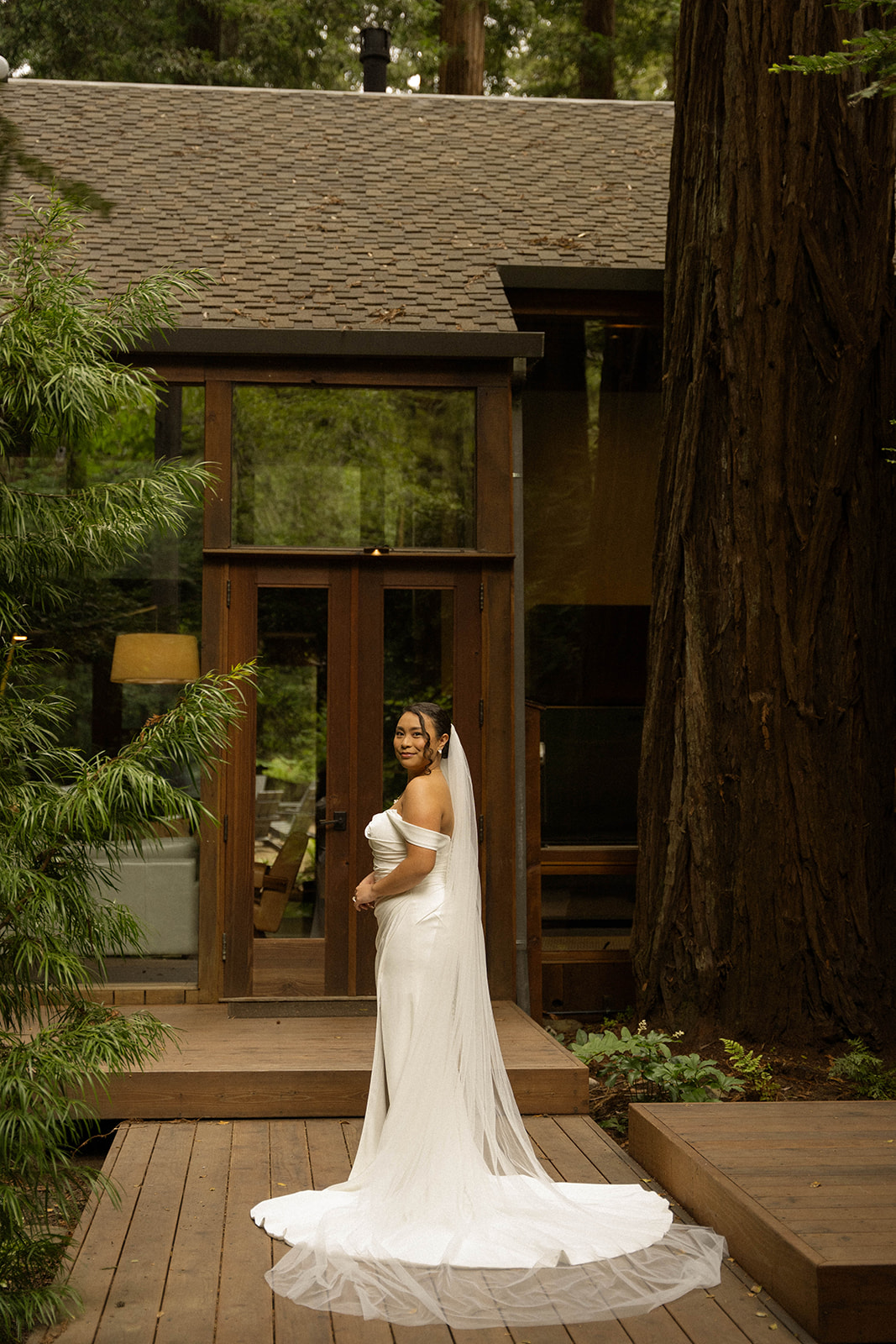 Bride in an off-shoulder gown posing in front of a rustic cabin at her intimate Big Sur wedding.