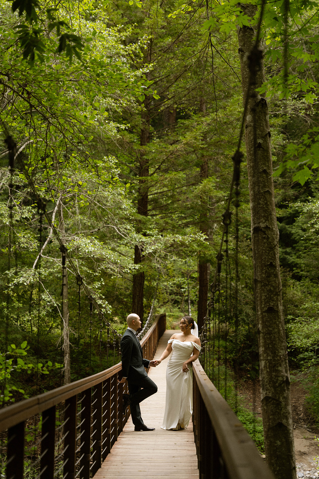 Bride and groom standing on a wooden bridge surrounded by lush trees during their Big Sur wedding at one of the most scenic Big Sur wedding venues.