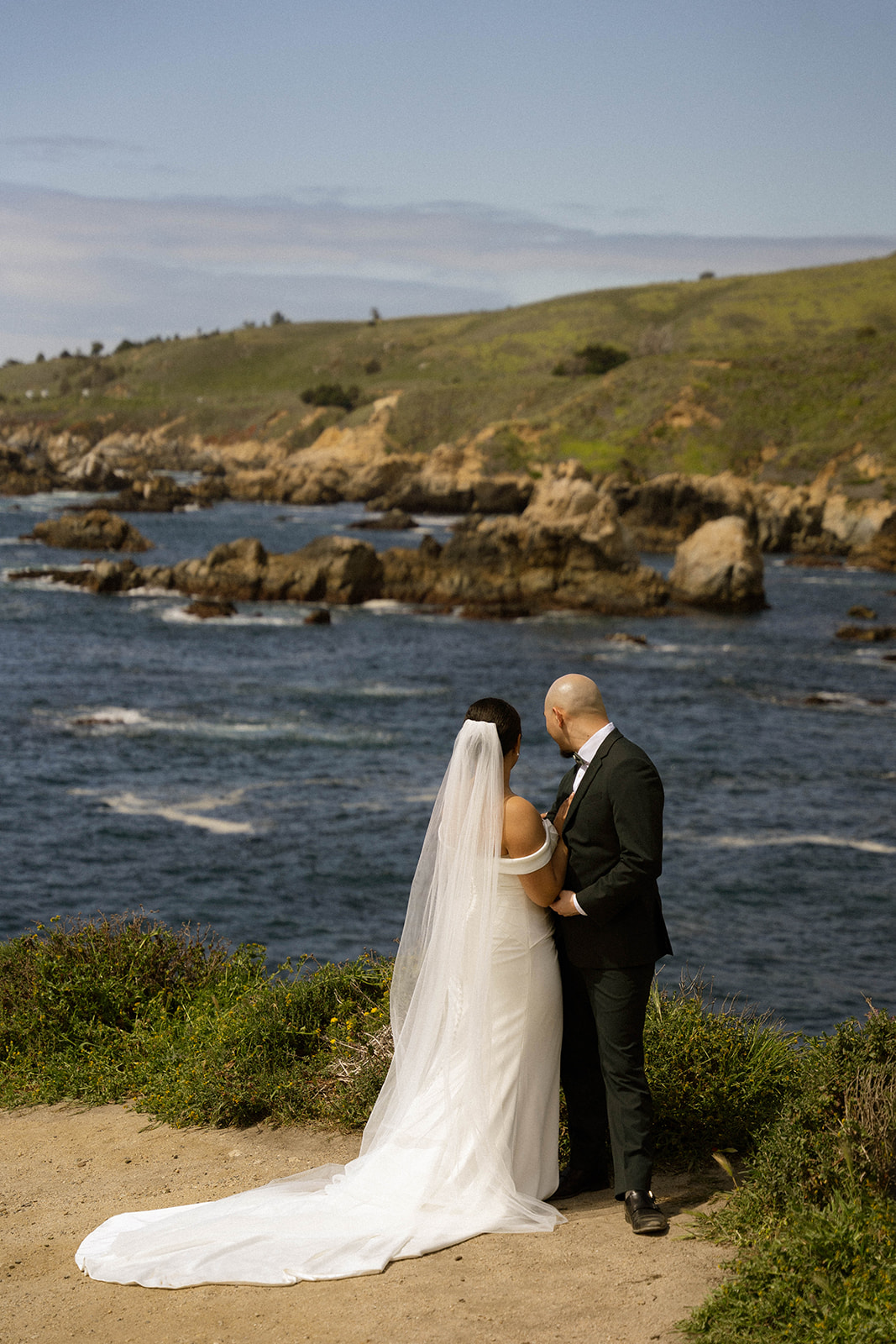 Couple standing together, gazing at the ocean from a cliffside, enjoying the view at their Big Sur wedding venue.
