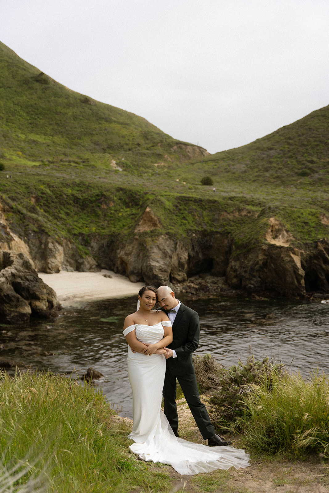 Bride and groom embracing near the rocky coastline at their Big Sur wedding portraits.