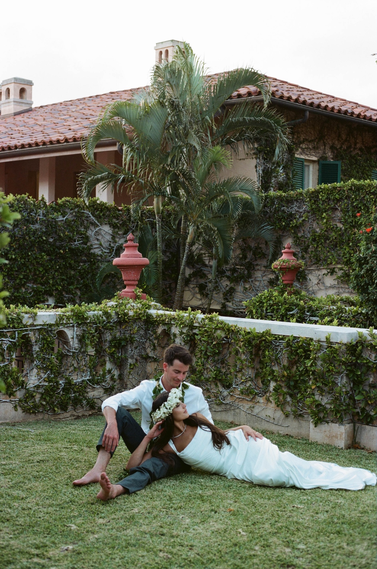 The groom sits barefoot on the grass as the bride lounges beside him, resting her head on his shoulder — captured by a destination wedding photographer.