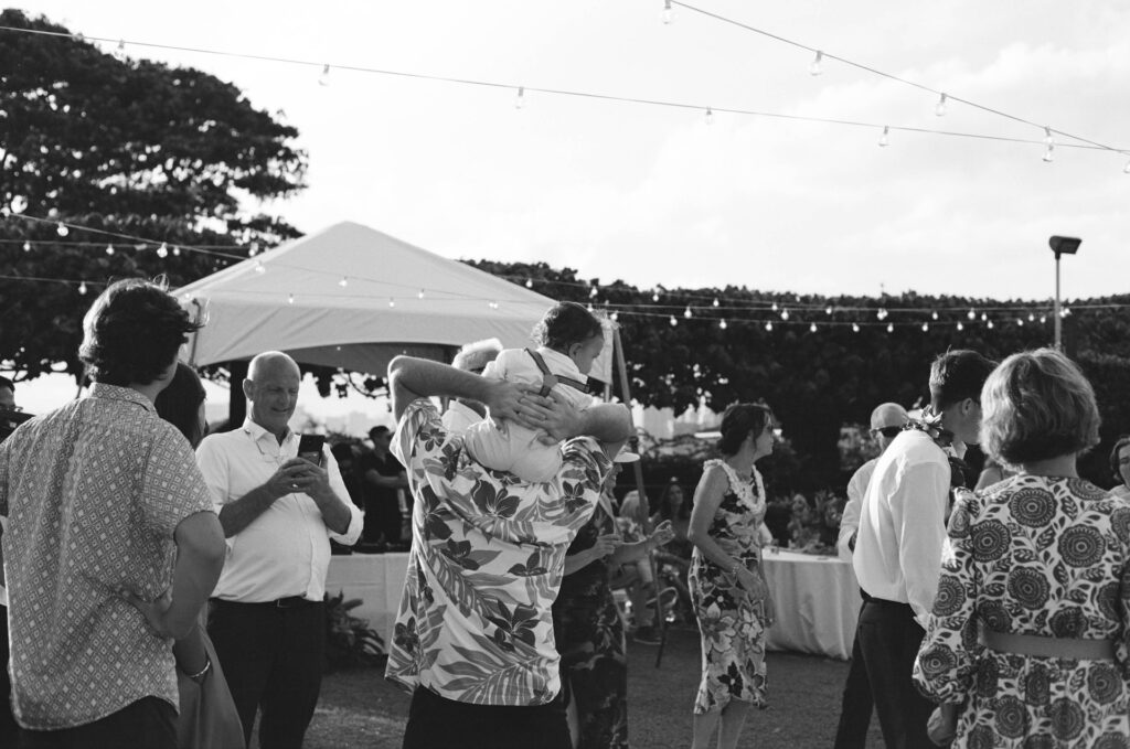 A joyful scene as a guest carries a toddler on his shoulders among a crowd dancing beneath string lights — a candid captured by a destination wedding photographer.