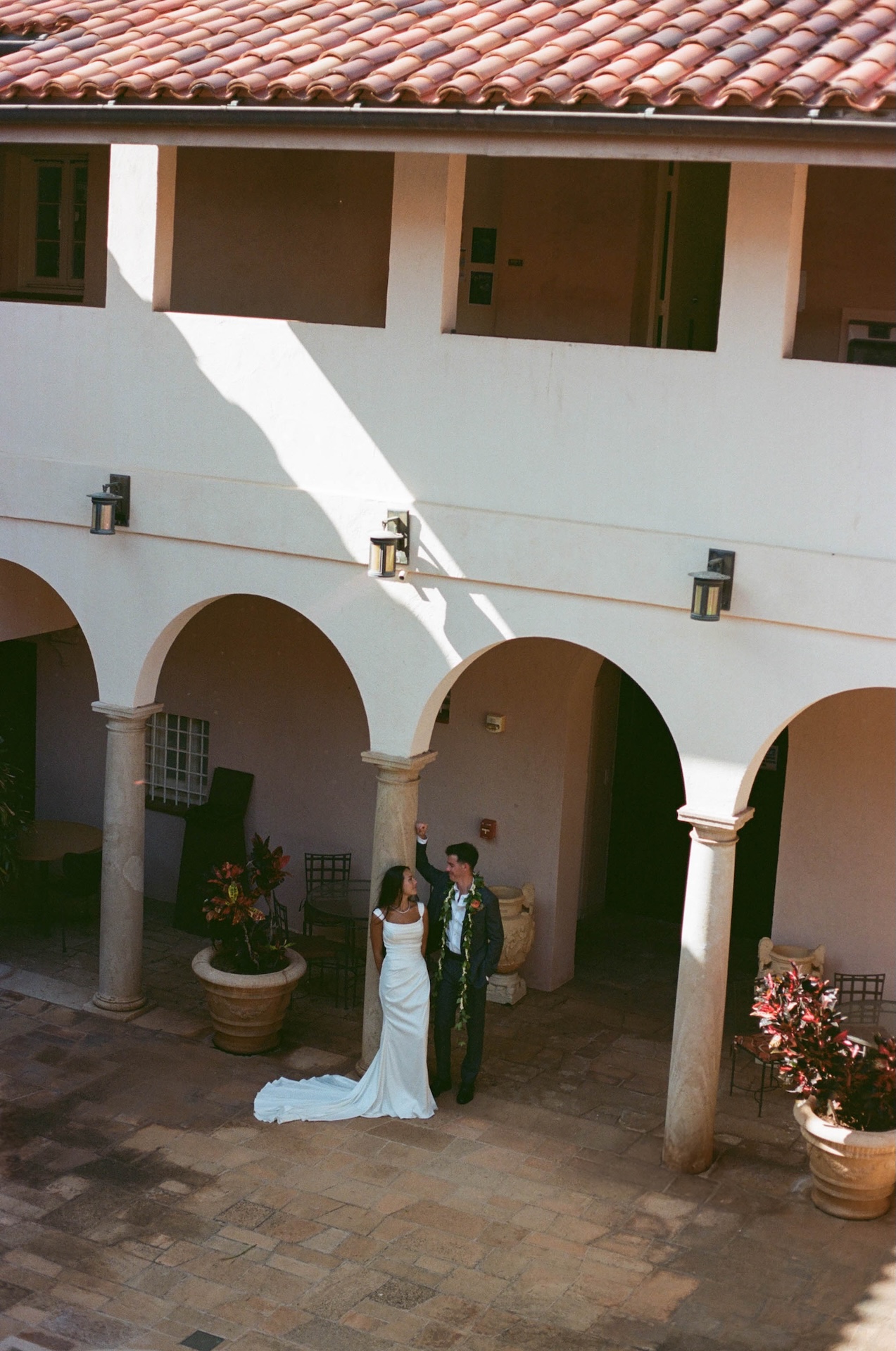 The couple dances beneath arched columns in a sun-drenched courtyard, the groom lifting the bride’s hand as she smiles — captured by a destination wedding photographer.