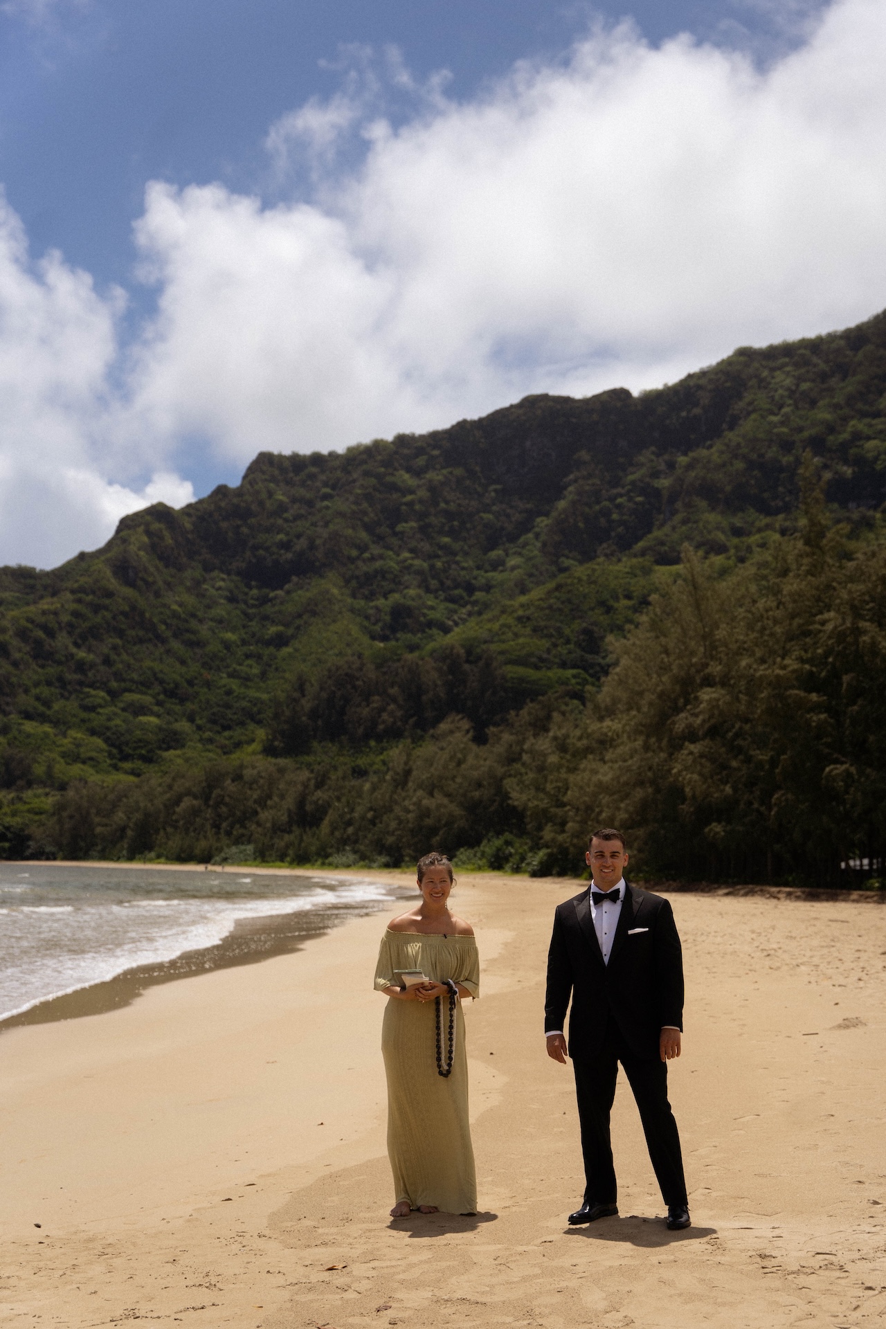 The officiant and groom standing at the end of the beach watching the bride approach them. 