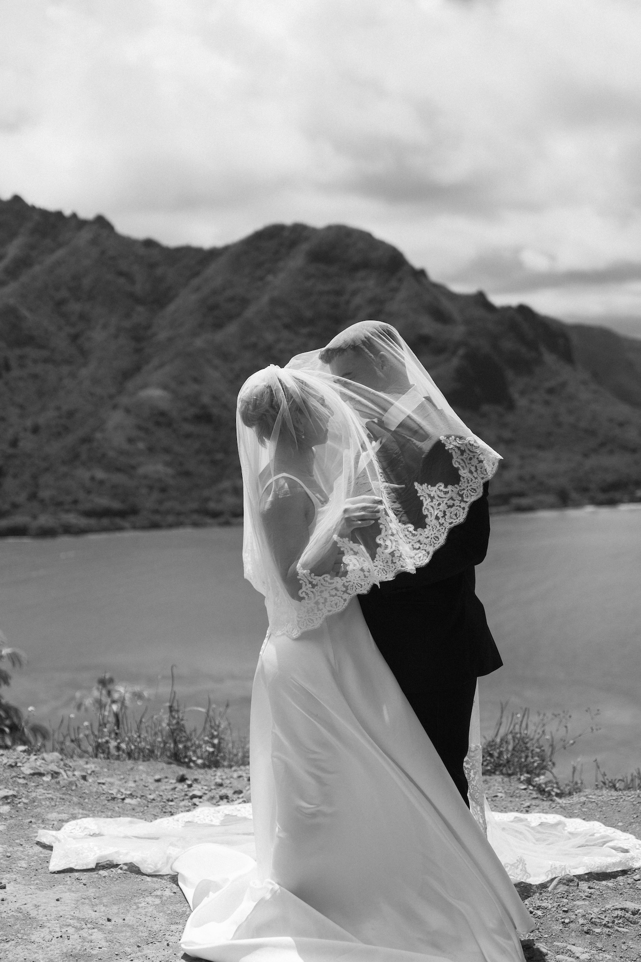 Bride and groom stare at each other lovingly under her lace-trimmed veil on a cliff overlooking the ocean — a breathtaking moment from their Hawaii airbnb wedding.