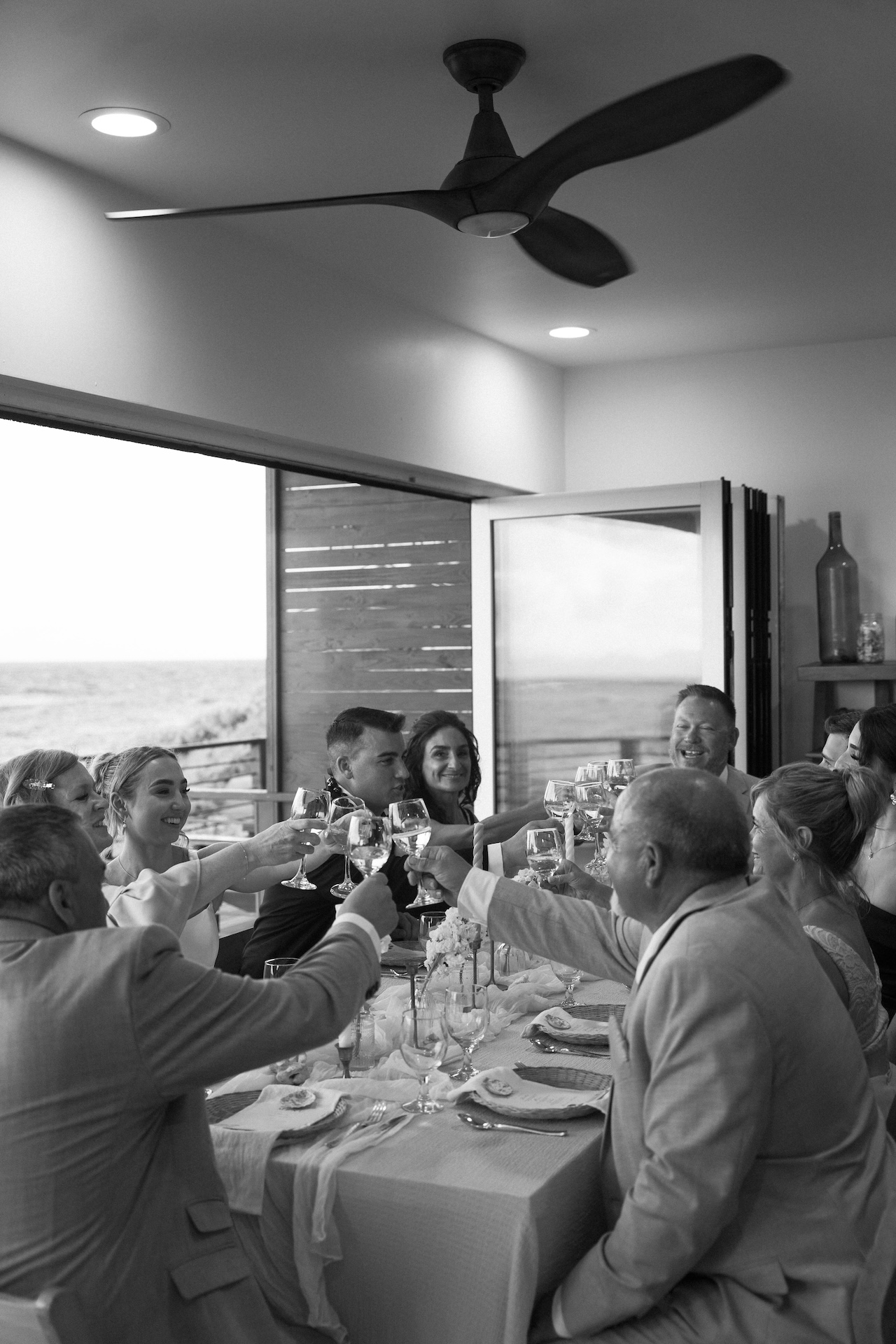 Friends and family raise their glasses for a toast, gathered inside for an airbnb wedding dinner full of joy and laughter.