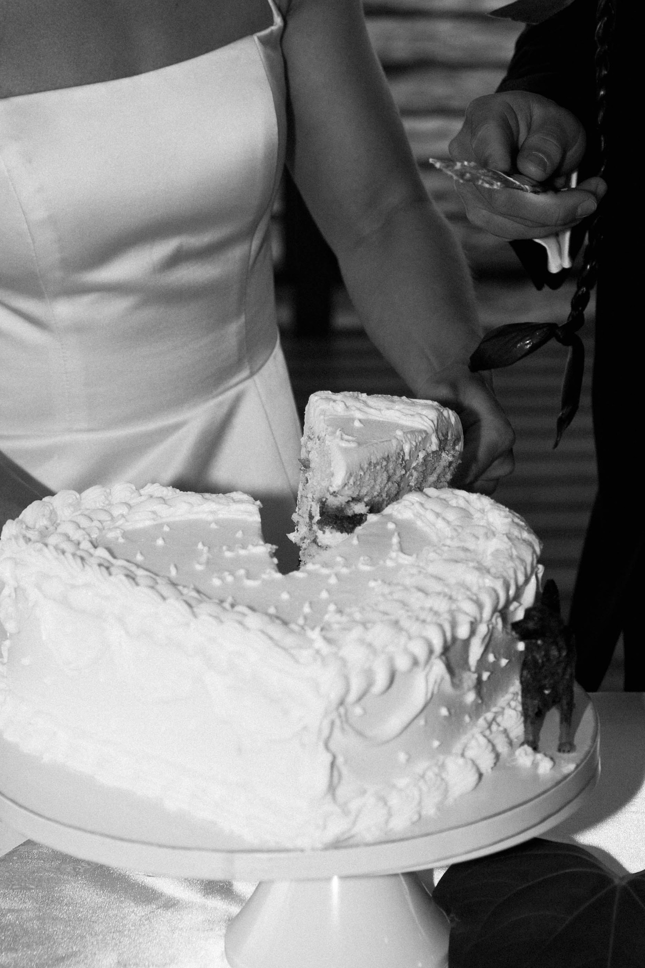 Close-up of the couple cutting a slice of their white wedding cake, showcasing delicate piping and joyful anticipation.