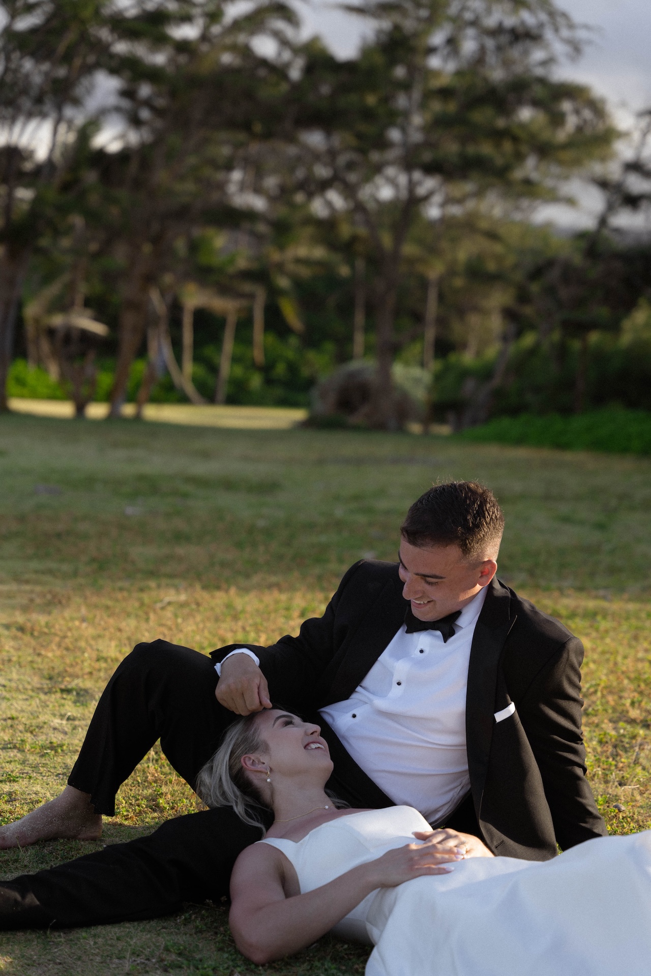 The bride and groom laying on the grass at their Airbnb wedding with the bride laying her head down on the grooms lap as they smile at each other. 