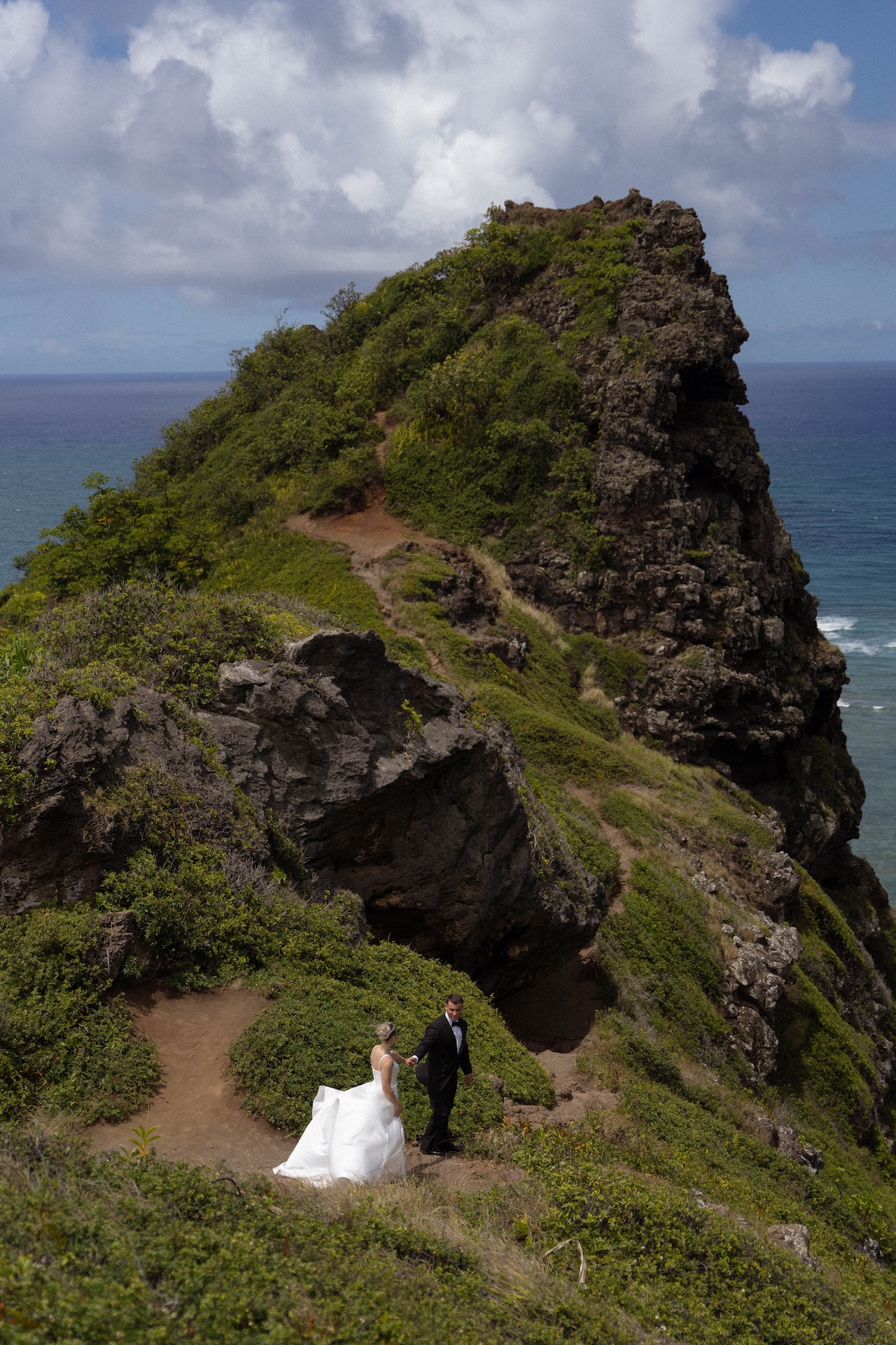 A dramatic trail leads around a rocky peak as the bride and groom walk hand in hand during their adventurous airbnb wedding portraits.