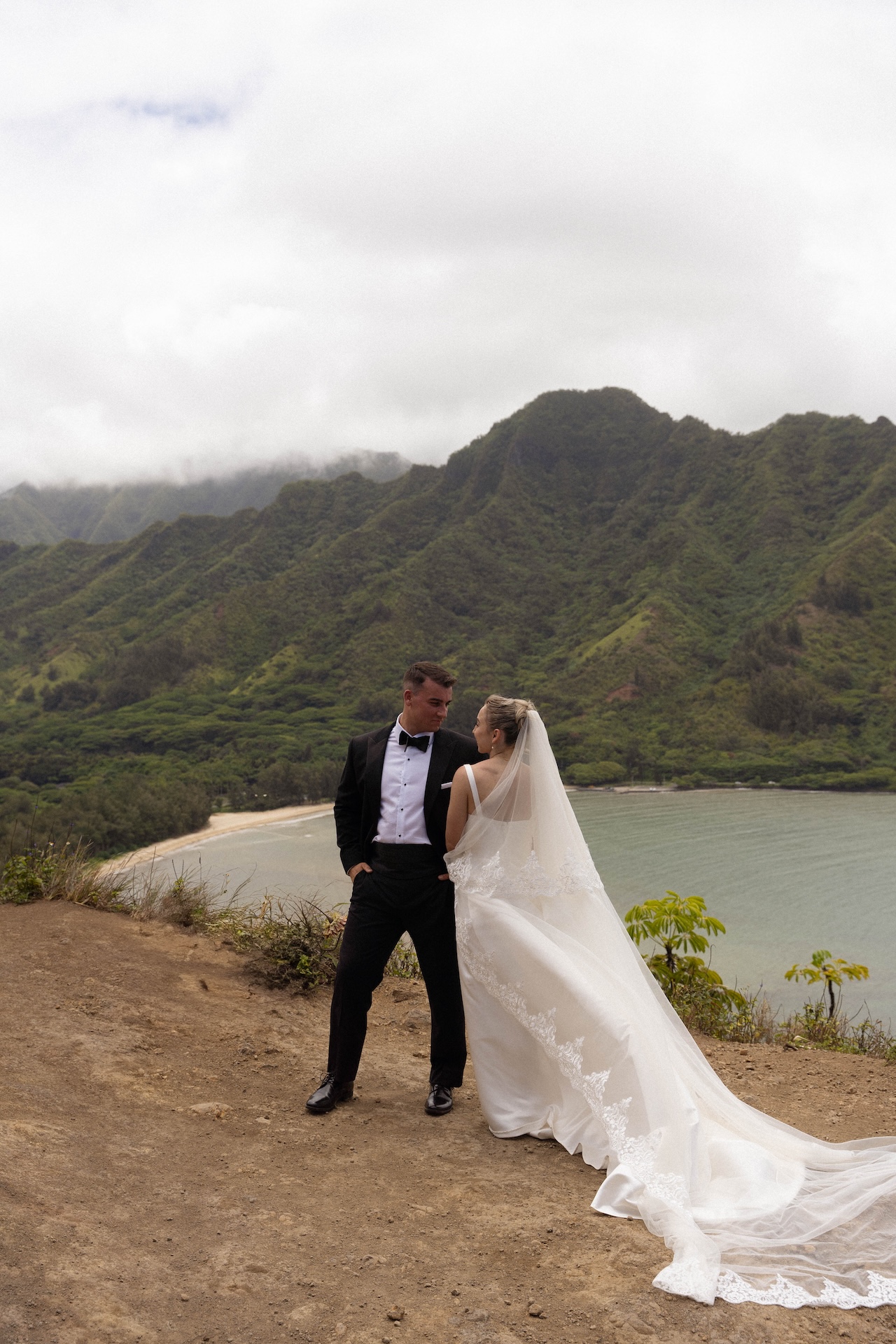 The couple poses on a coastal cliffside with sweeping views of the mountains and ocean behind them.