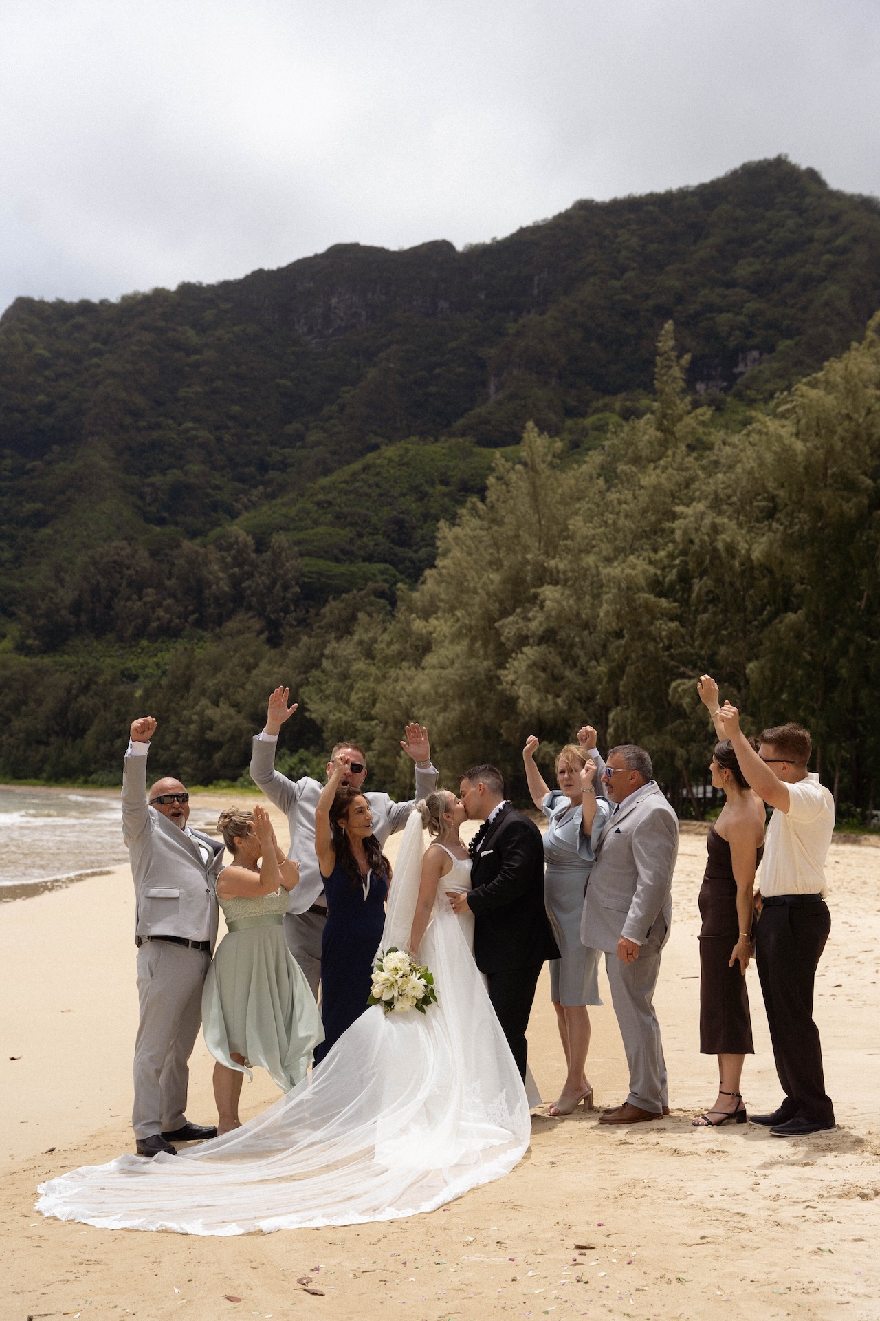 Bride and groom sharing a kiss as their friends and family cheer around them during their intimate airbnb wedding in Hawaii.