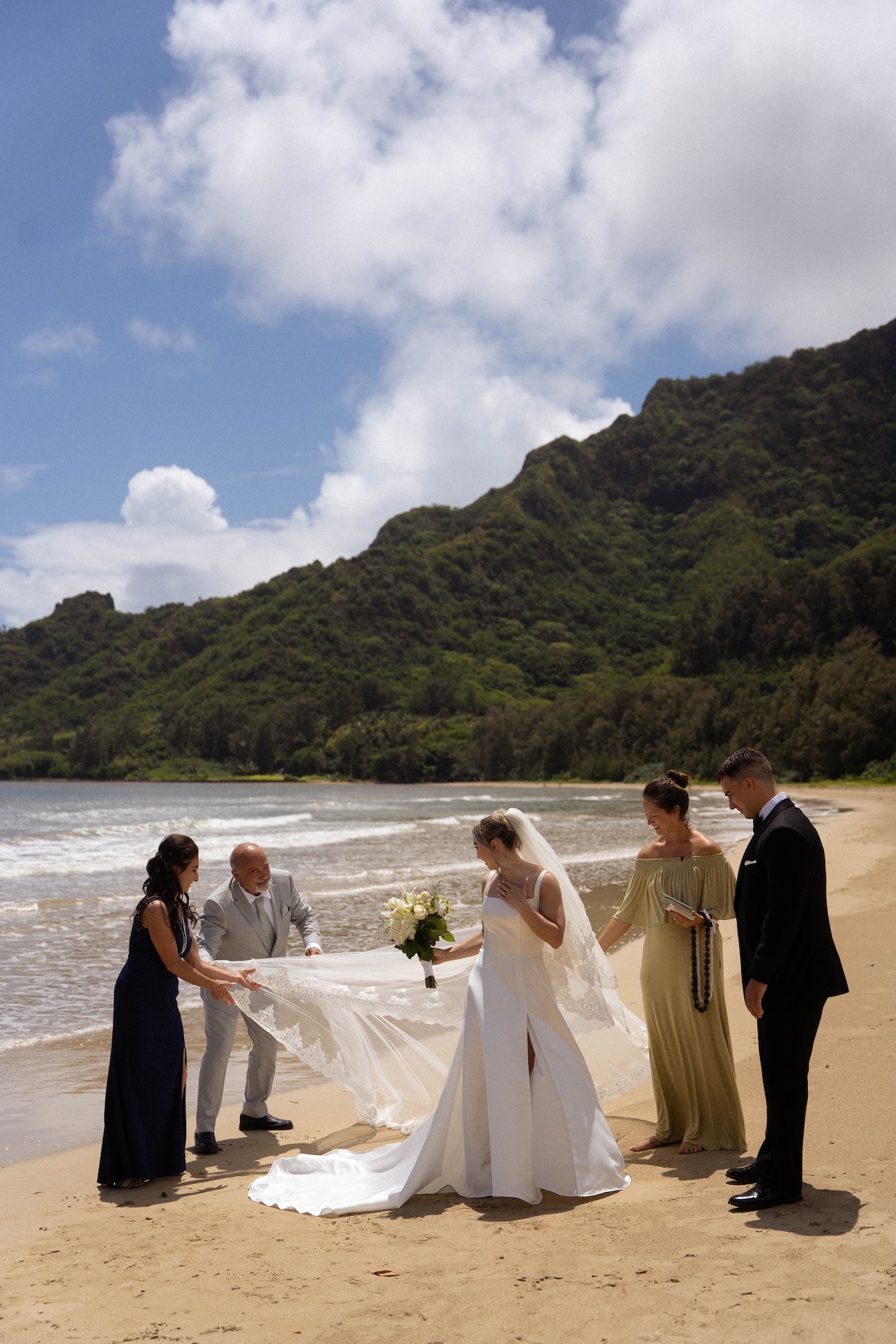 Friends and family help arrange the bride’s long lace veil on the beach just before the ceremony begins.
