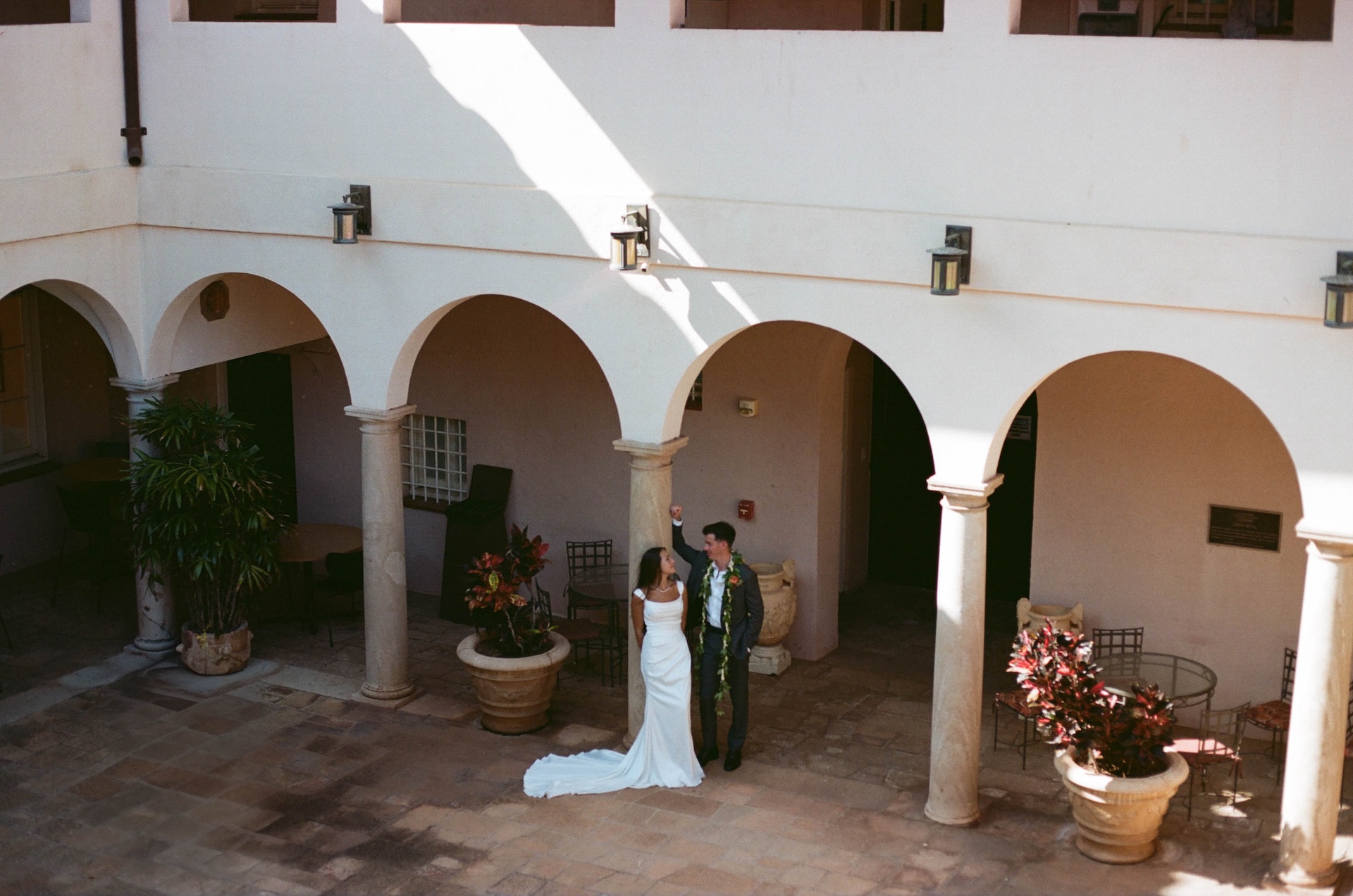 A wide view of the bride and groom dancing in an open-air courtyard, framed by stone columns and arches, captured by a destination wedding photographer.