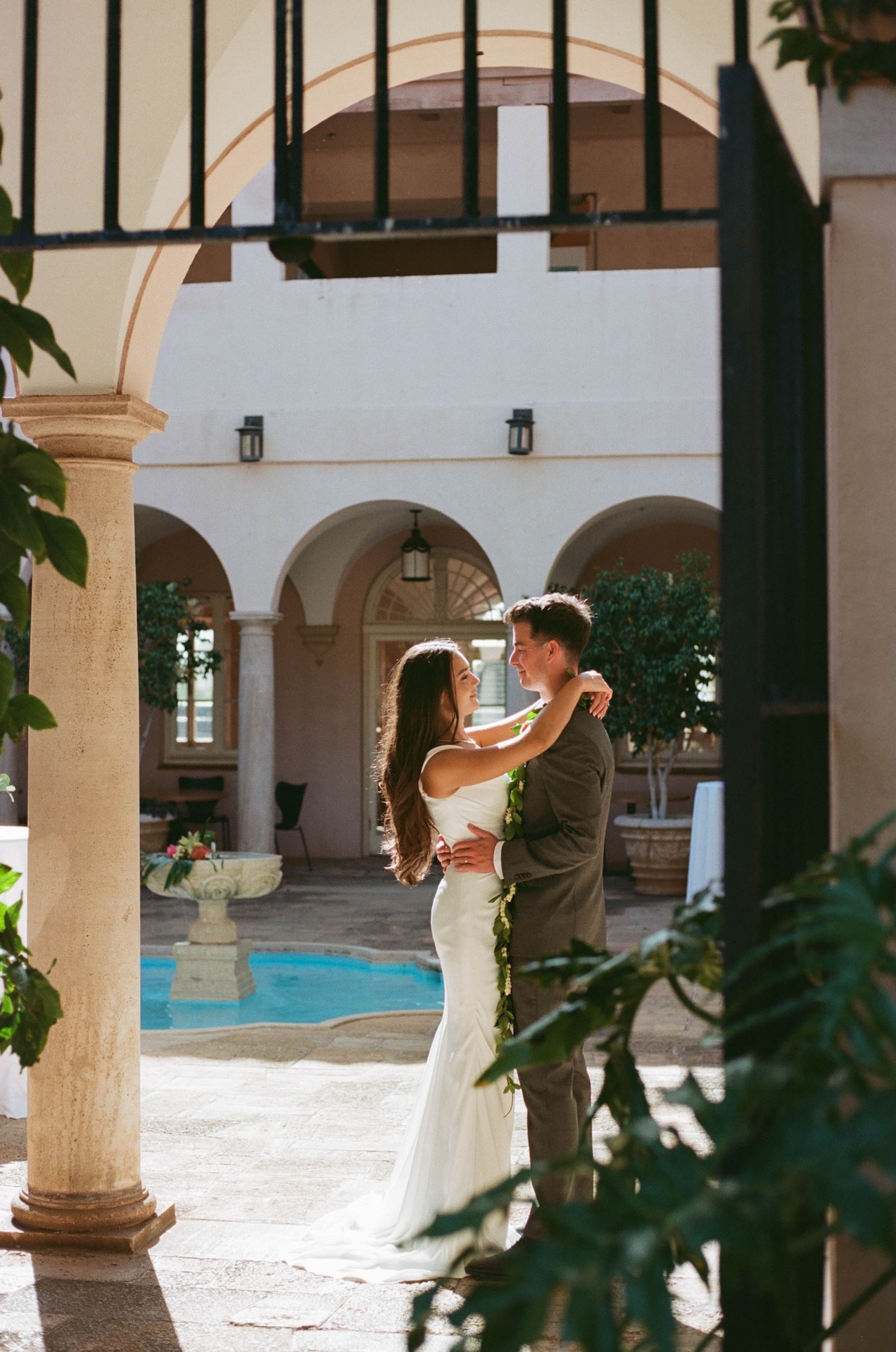 A sweet embrace between the couple as they dance near a courtyard pool, light filtering through the leaves.
