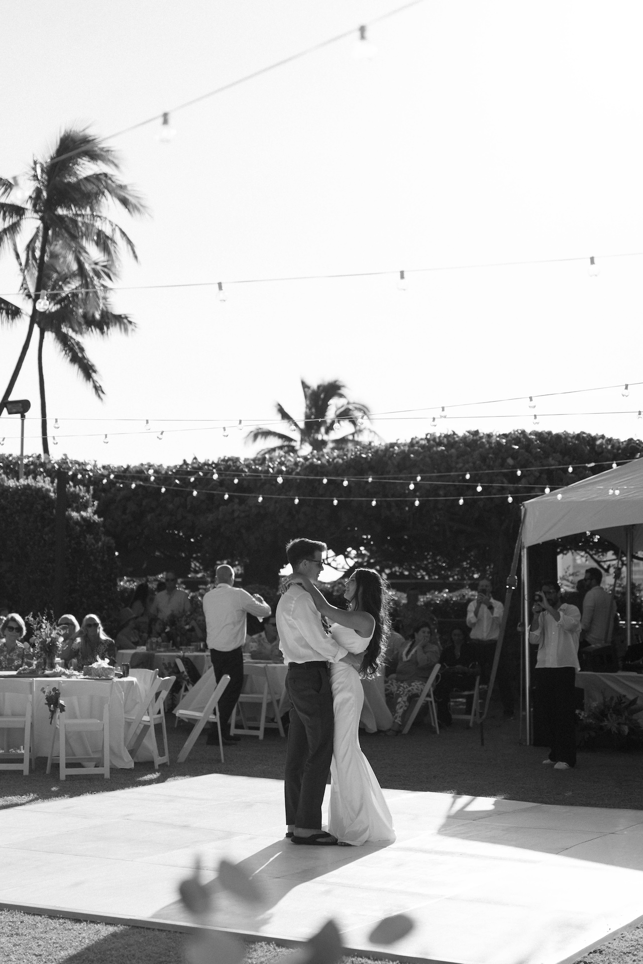 Another black and white moment of the couple dancing under twinkle lights, guests in the background and soft island light filling the scene — captured by a destination wedding photographer.
