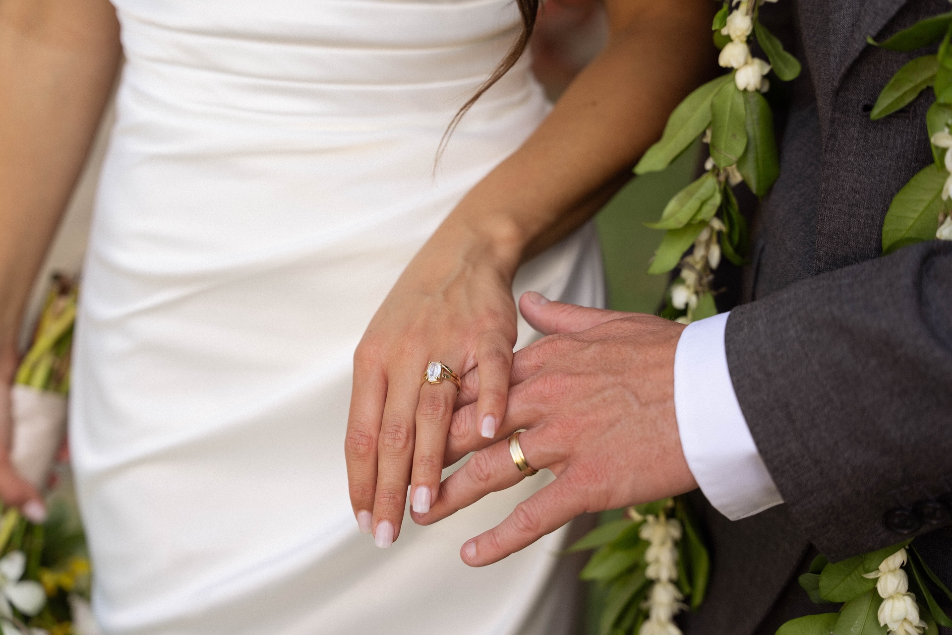 A close-up of the couple’s hands showing off their gold wedding bands, the bride’s emerald-cut ring sparkling against her white gown.