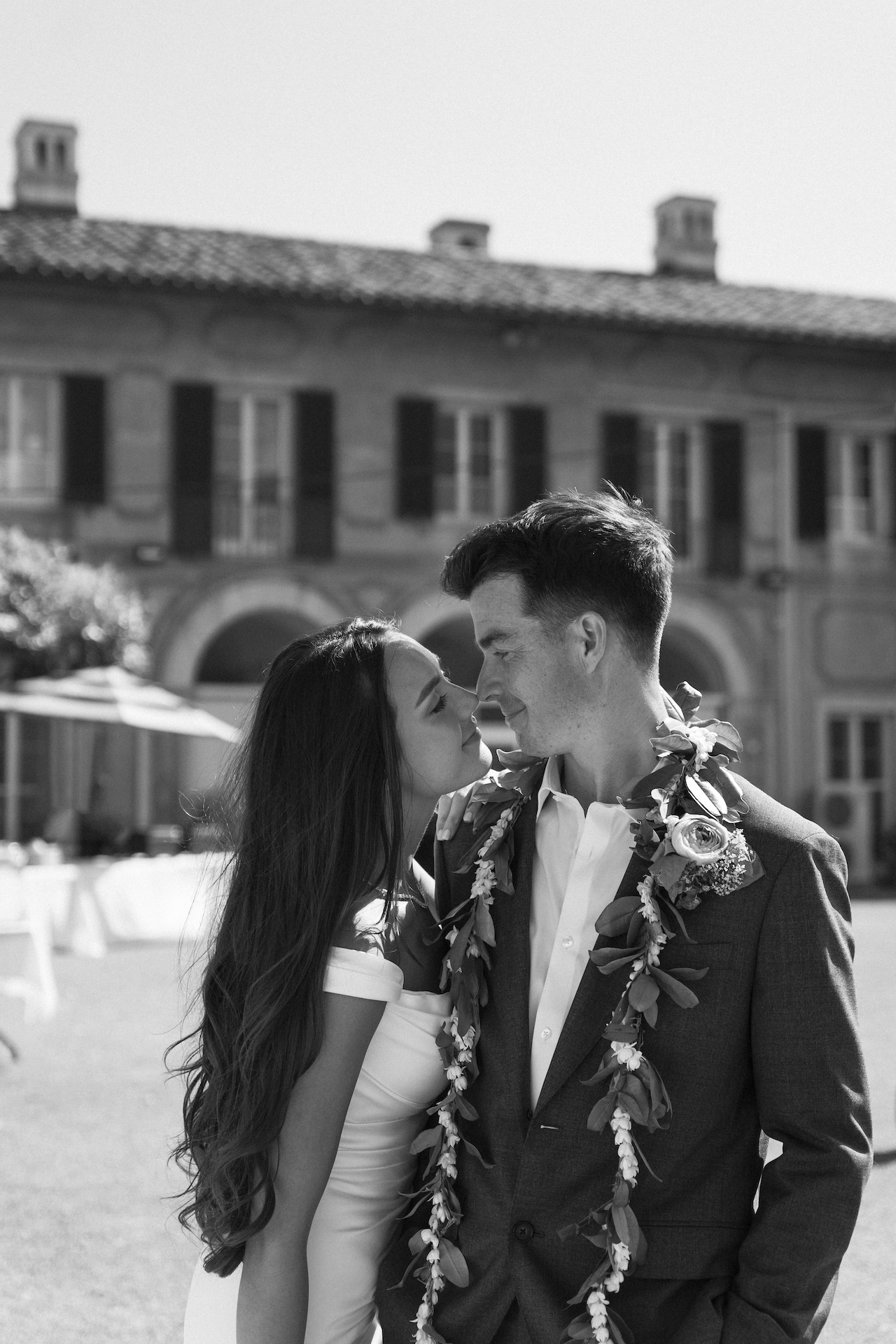 A close-up black and white moment of the couple smiling just before a kiss, set in front of a historic estate — a candid moment by a destination wedding photographer.