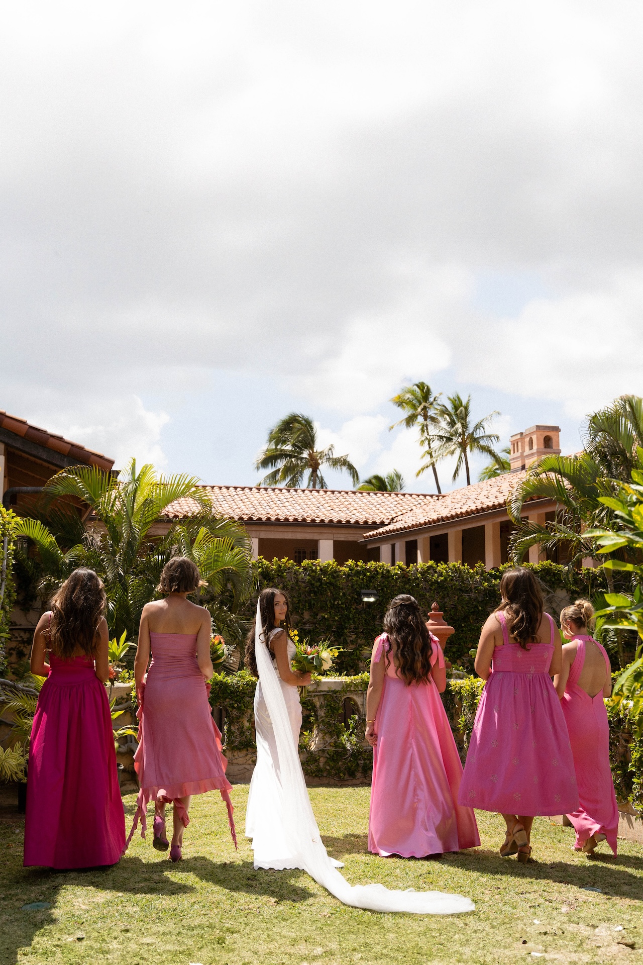 A group of bridesmaids walk with the bride through a sunny courtyard, her veil flowing behind her — a colorful moment captured by a destination wedding photographer.
