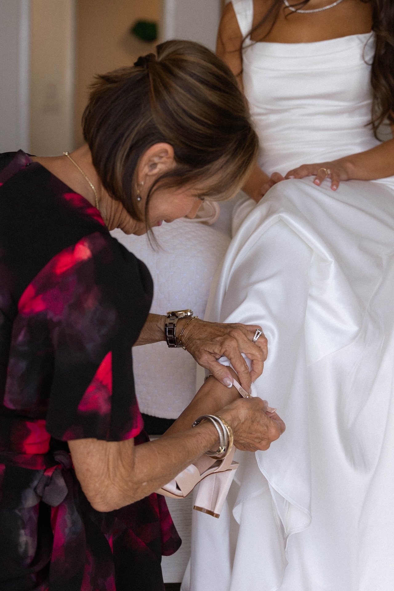 A close-up of the bride’s grandmother fastening the ankle strap of a blush pink heel on the bride’s foot.