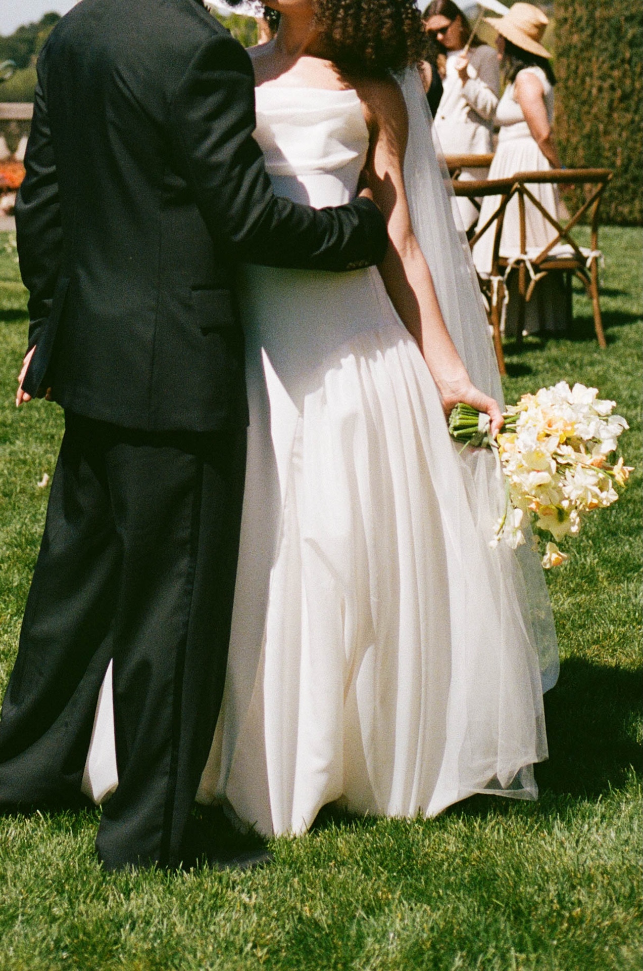 A candid moment of the bride holding her bouquet while embraced by the groom in the garden after the ceremony at their wedding estate venue.

