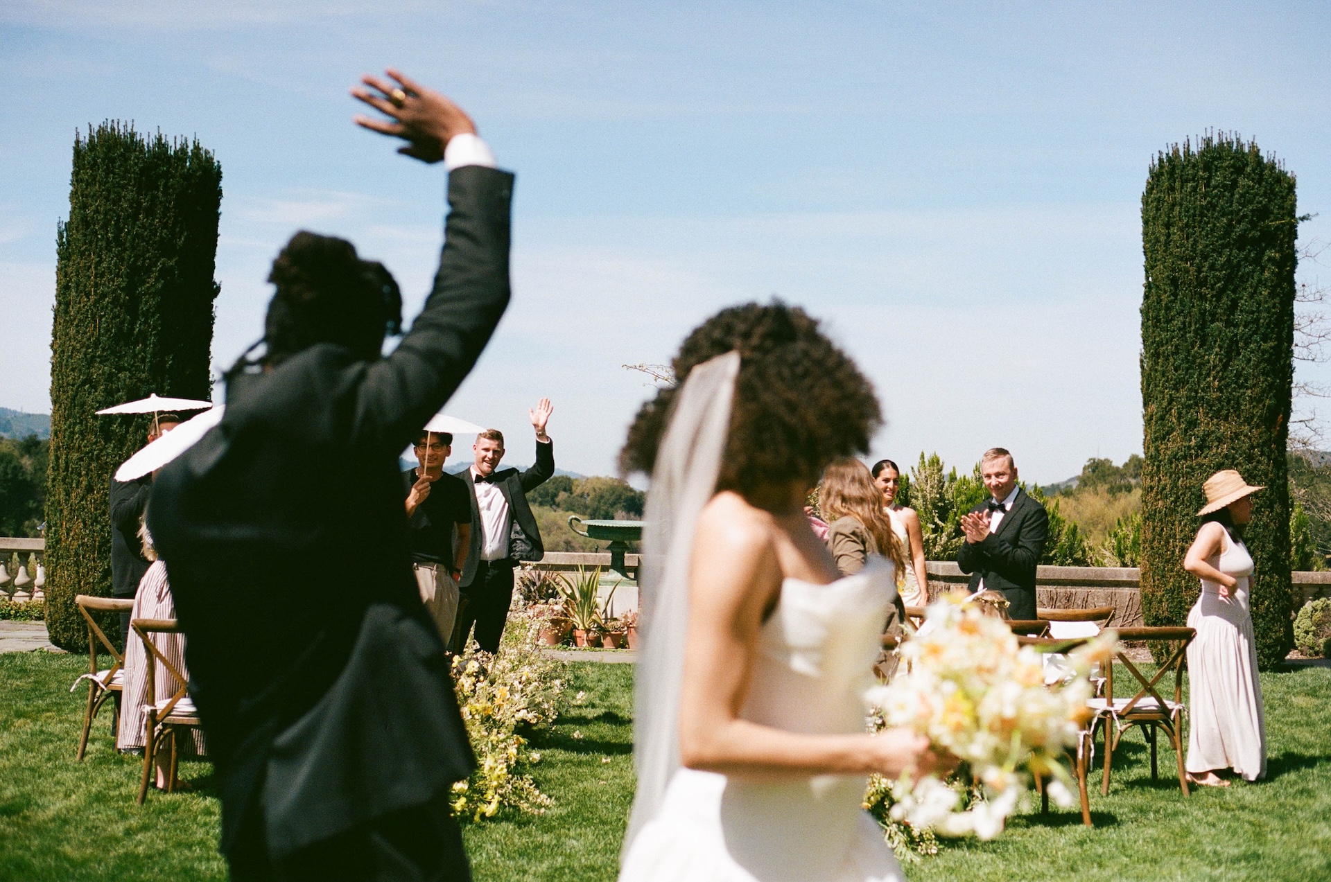 The bride and groom waving to guests after their ceremony, capturing a candid joyful moment.

