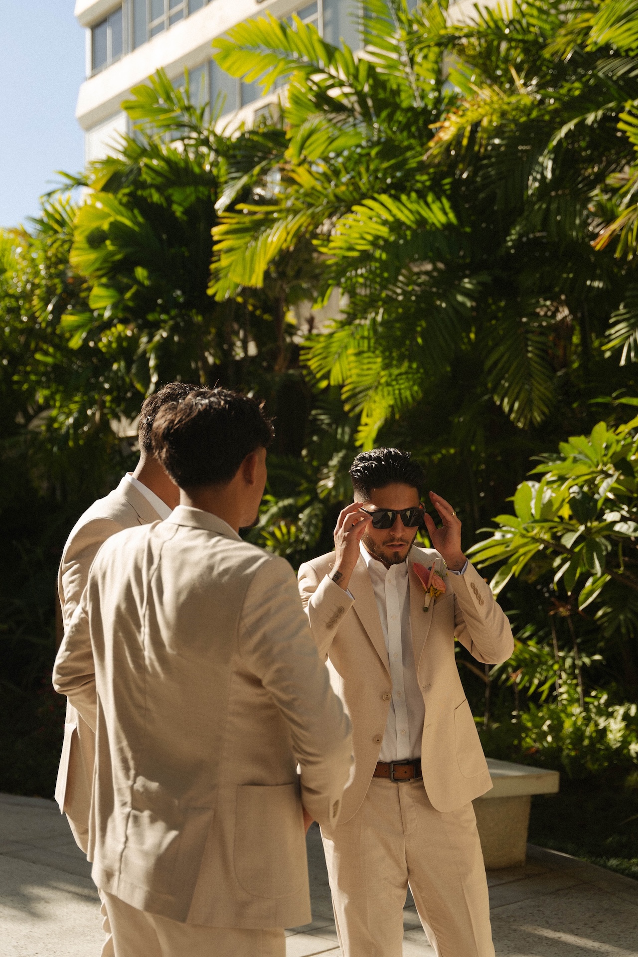 Groomsmen hanging out in a sunny garden, with the groom adjusting his sunglasses before the ceremony at their destination wedding in Hawaii.

