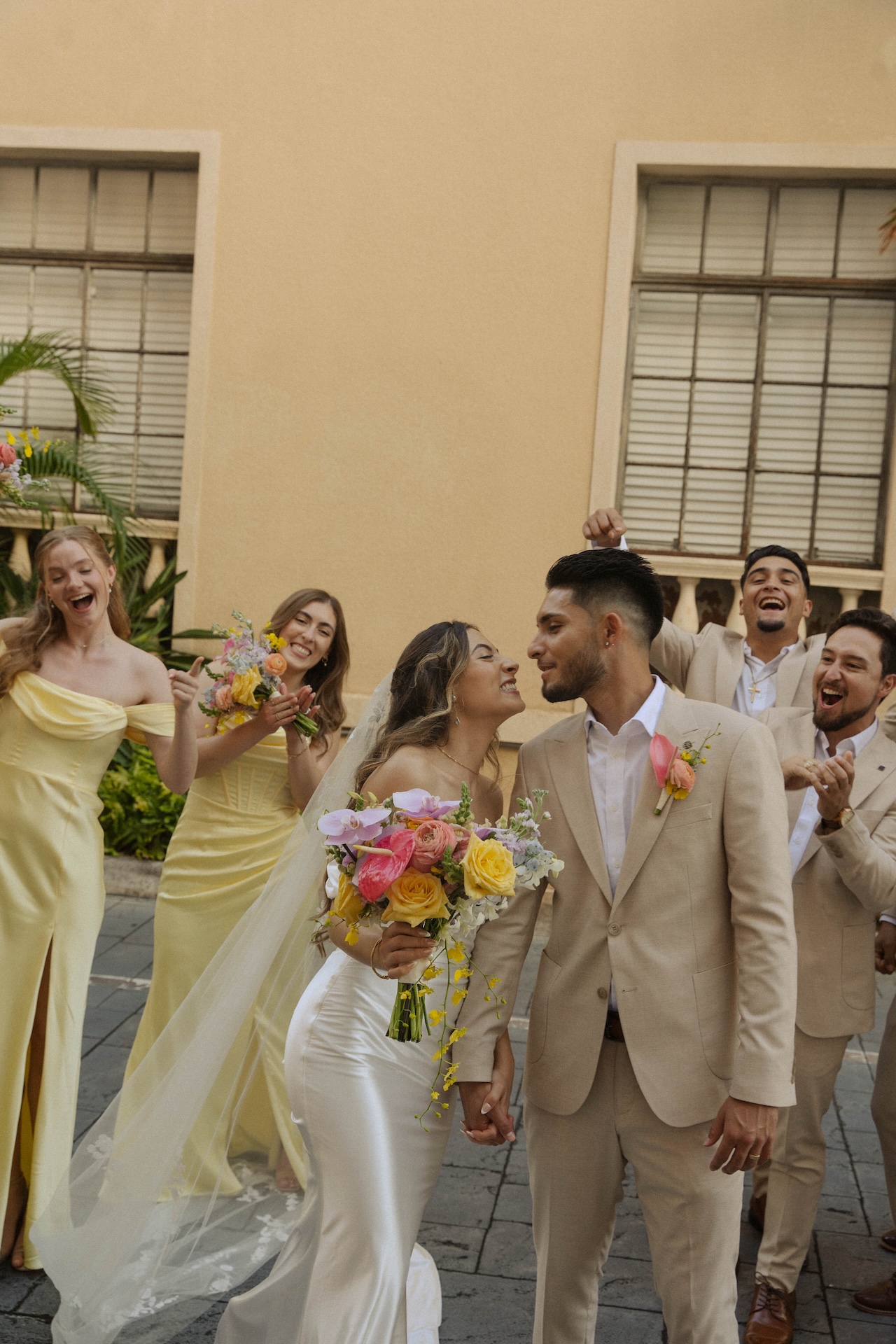 Bride and groom celebrating with their bridal party, laughing and holding hands.

